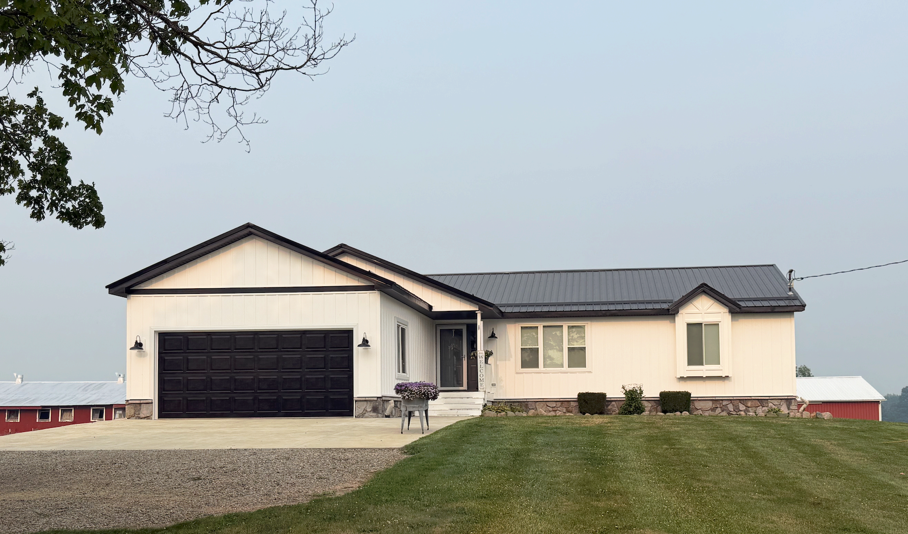 Single-story house with attached garage on a gravel driveway, set on a grassy lot under an overcast sky.