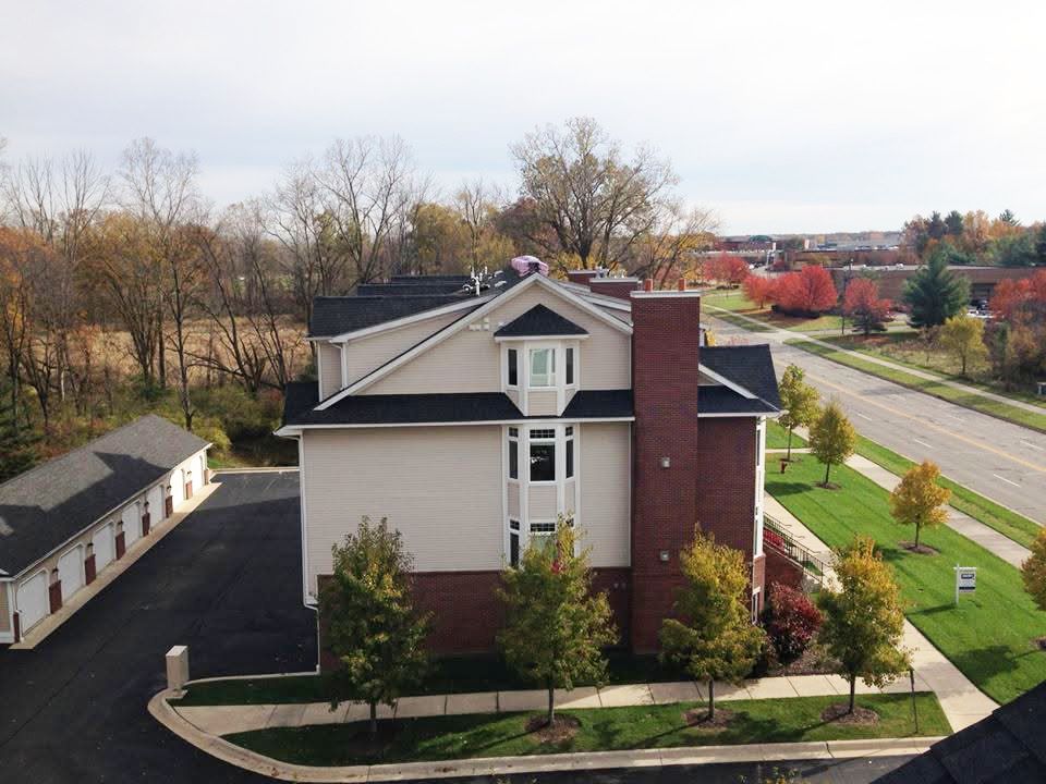 Aerial view of a beige house with a brick chimney, trees, and a road in autumn.