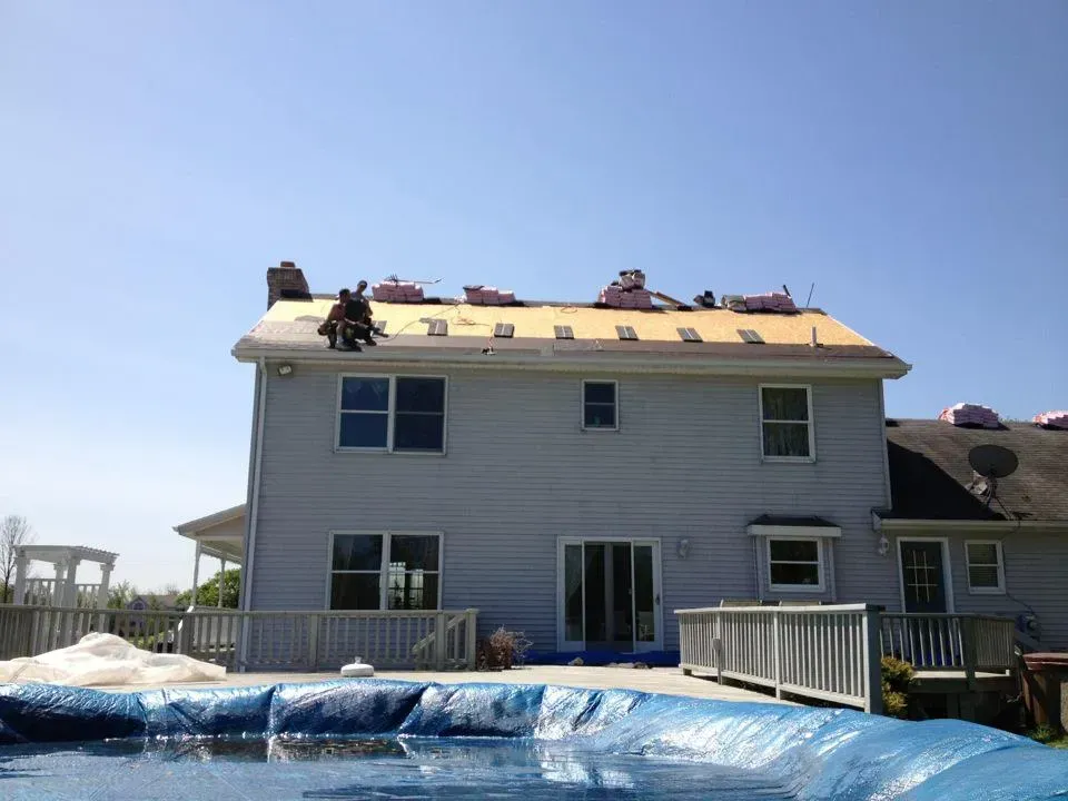 Two-story house with workers on the roof, covered by blue tarps during repairs