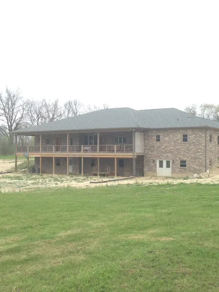 Large two-story brick house under construction with a covered porch and grassy yard.