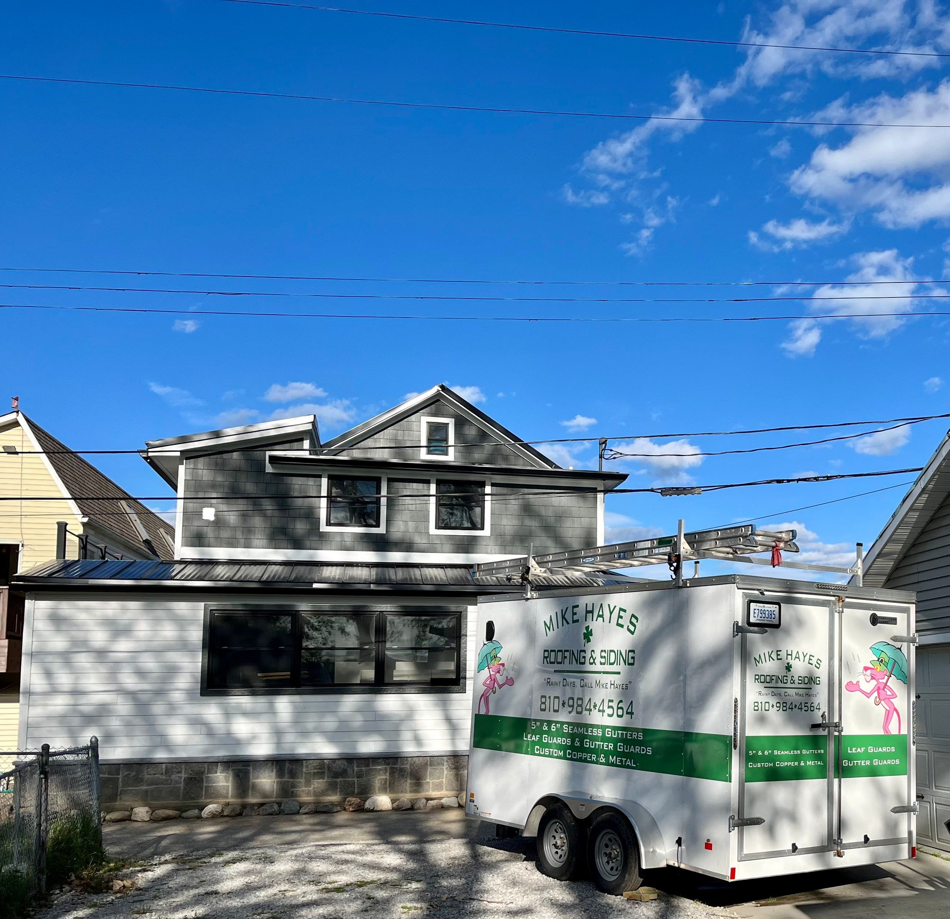 White trailer with green stripe parked in front of a house under a bright blue sky