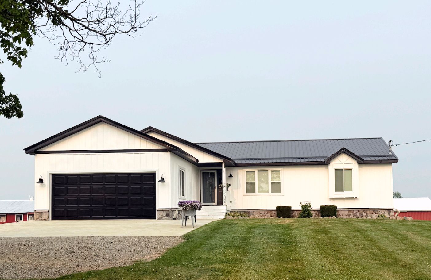 Single-story white house with black garage door and green lawn under a gray sky