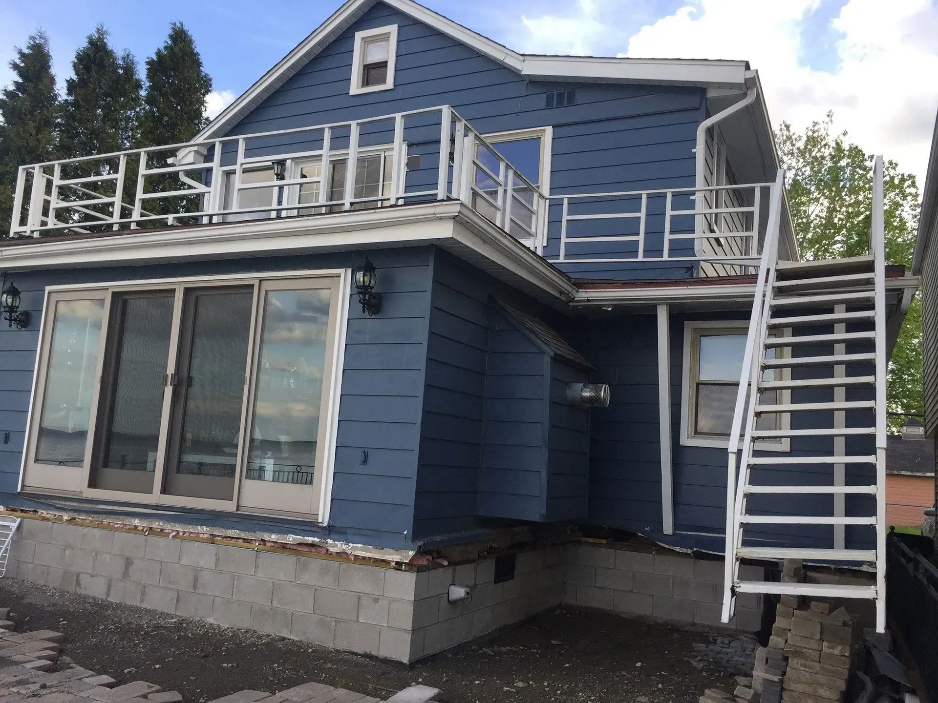 Blue house with rooftop deck and exterior staircase, viewed from outside.