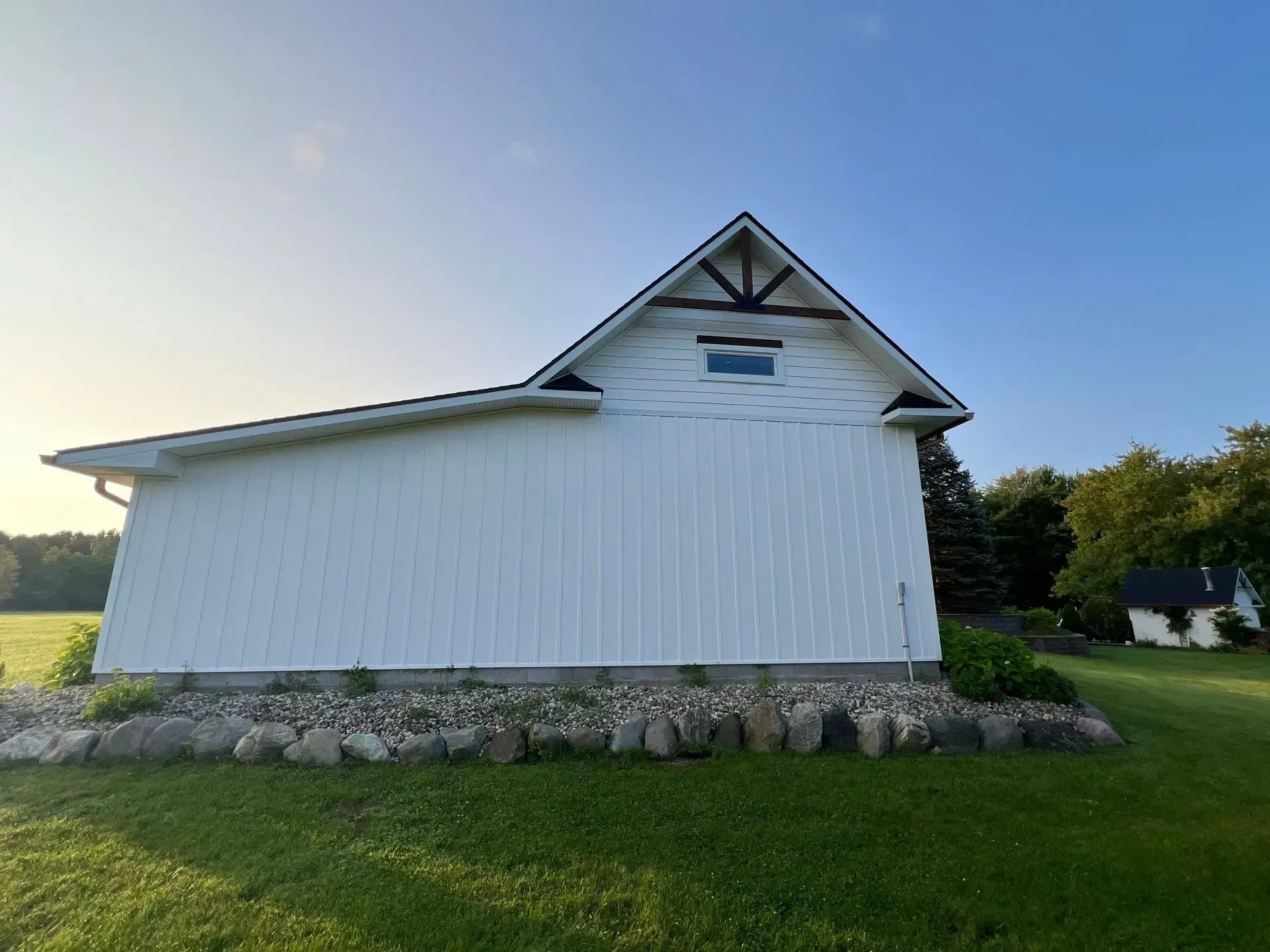 White barn with stone foundation on a grassy field under a clear blue sky.