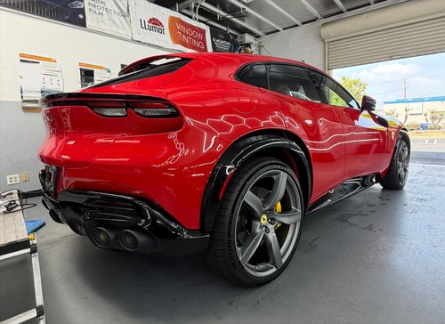 Red sports SUV on a lift in an auto shop, rear view with black wheels and quad exhausts