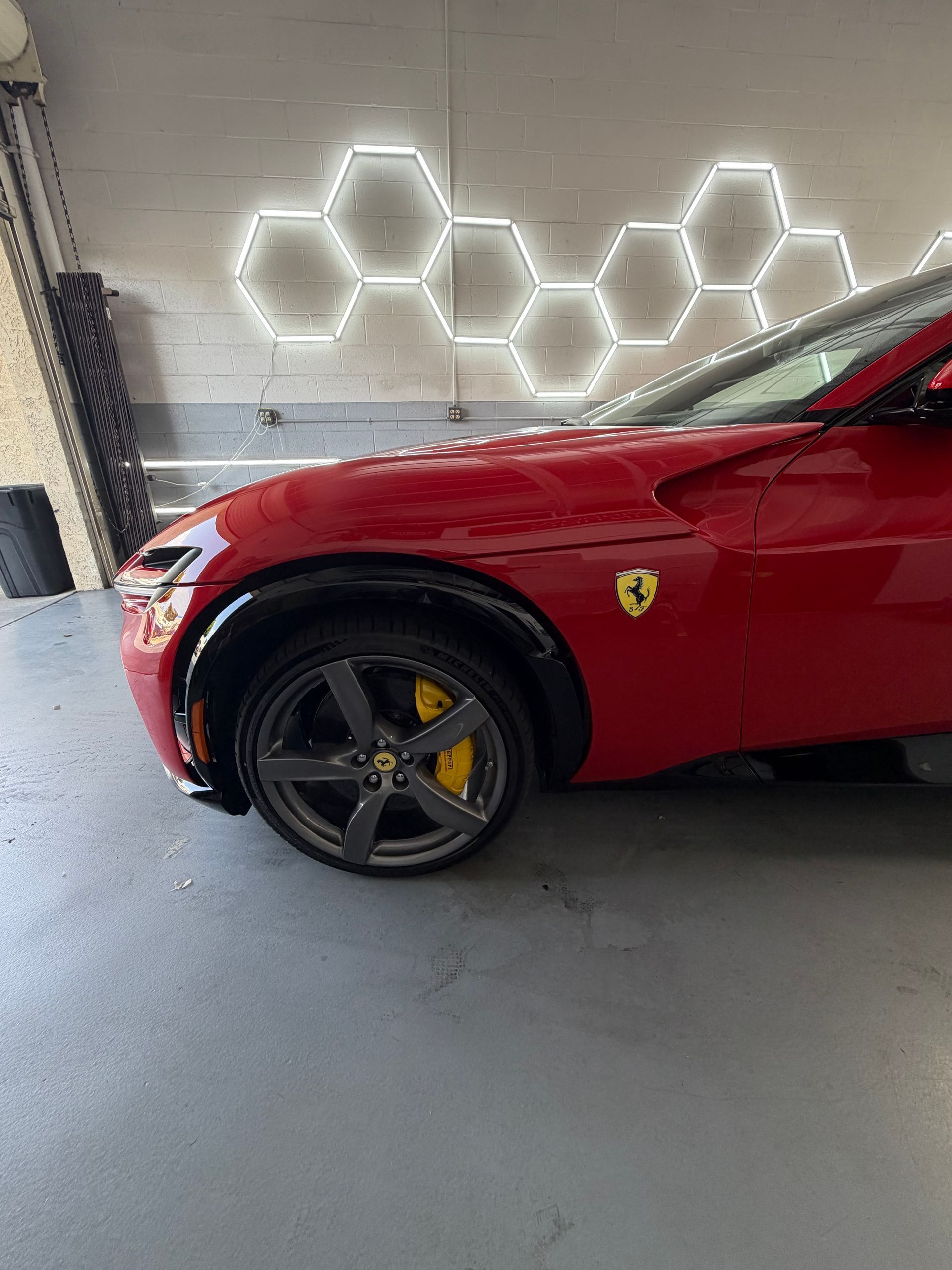 Red Ferrari parked in a garage beside glowing hexagon wall lights