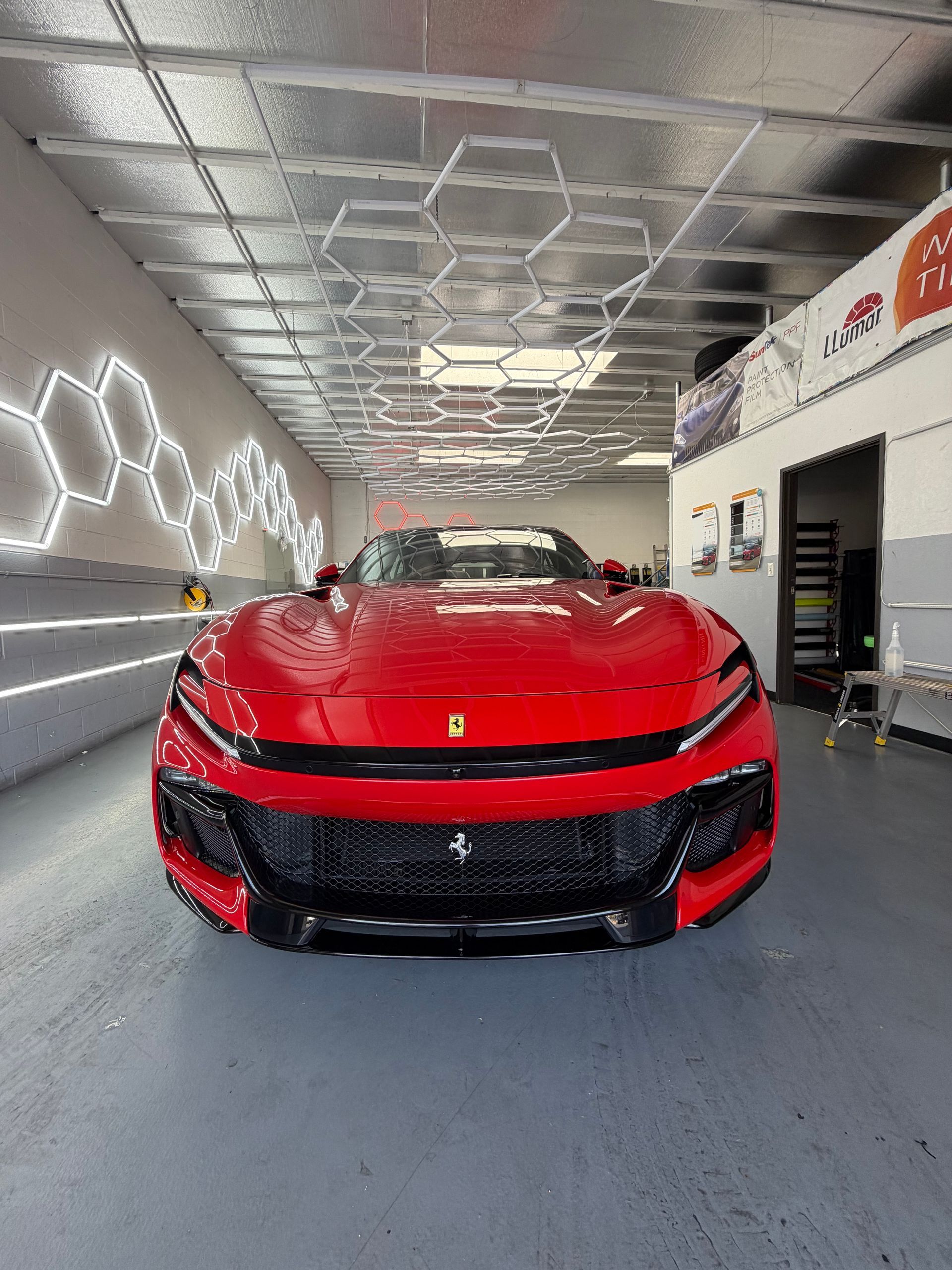 Red sports car in a modern showroom, front view with bright lights and geometric ceiling.