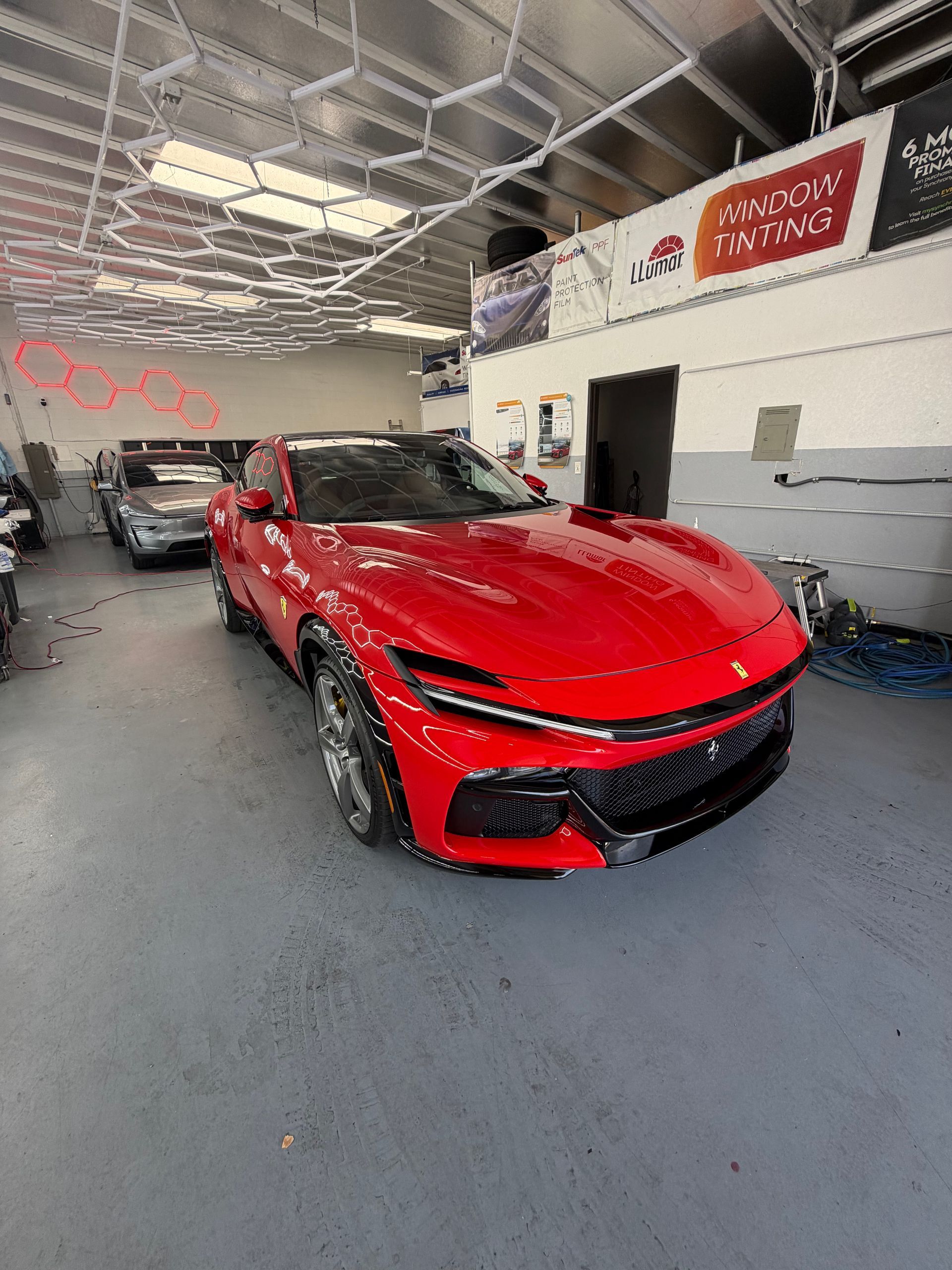 Red sports car in an auto shop with a high ceiling and another car in the background