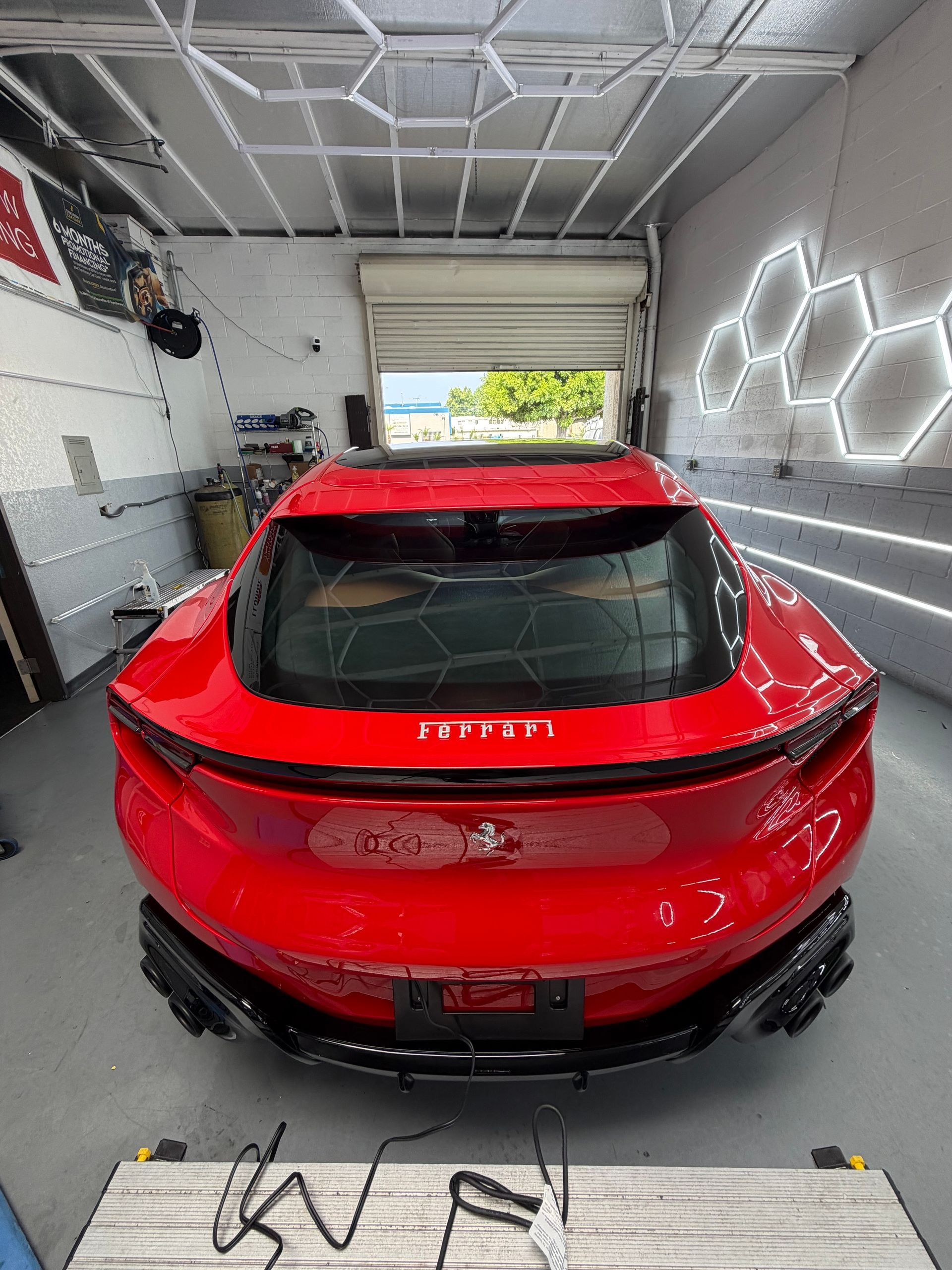 Red sports car parked in a modern garage with bright hexagonal wall lights and an open door.
