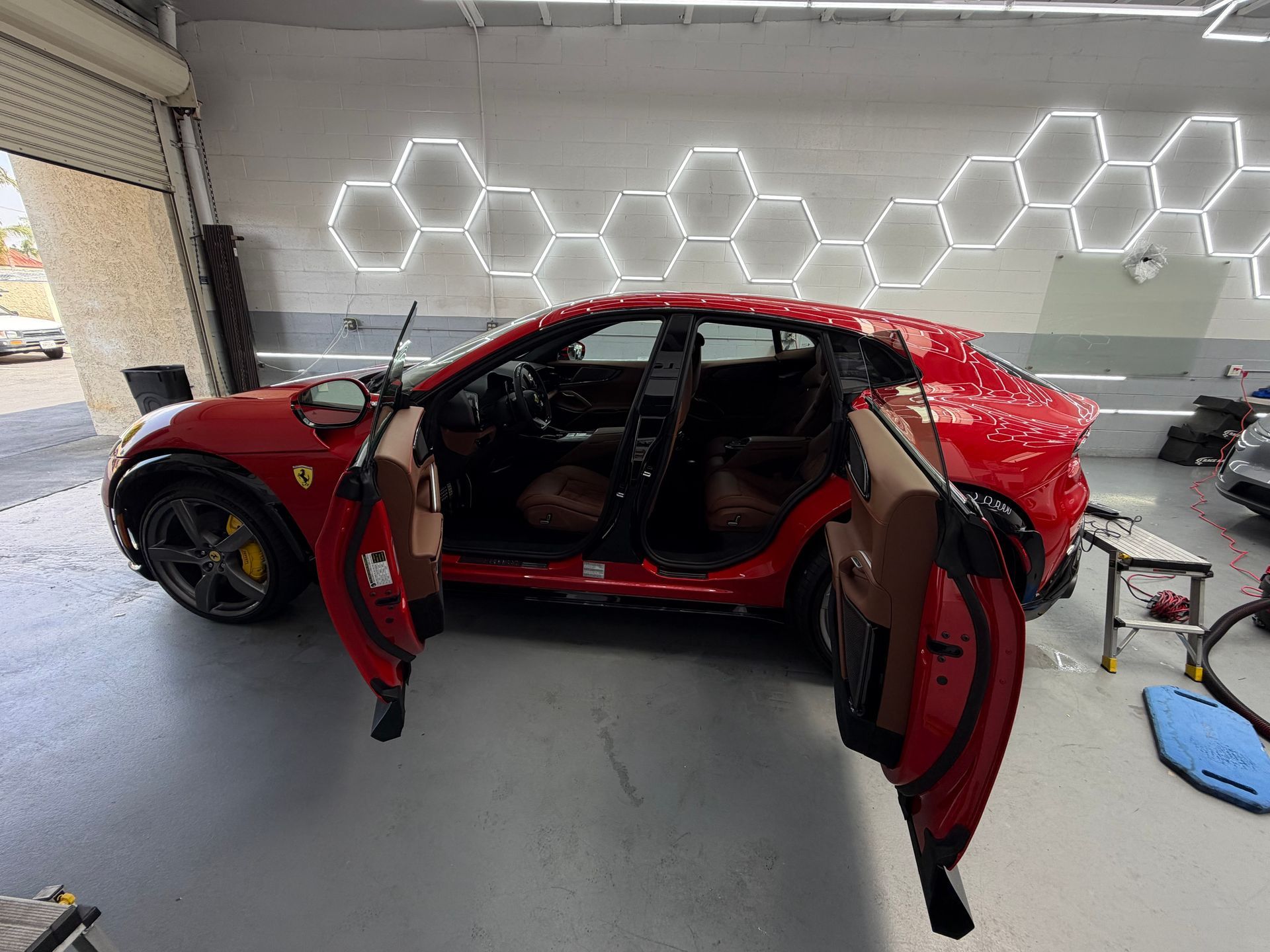 Red sports car with both doors open in a garage, viewed from the front side.
