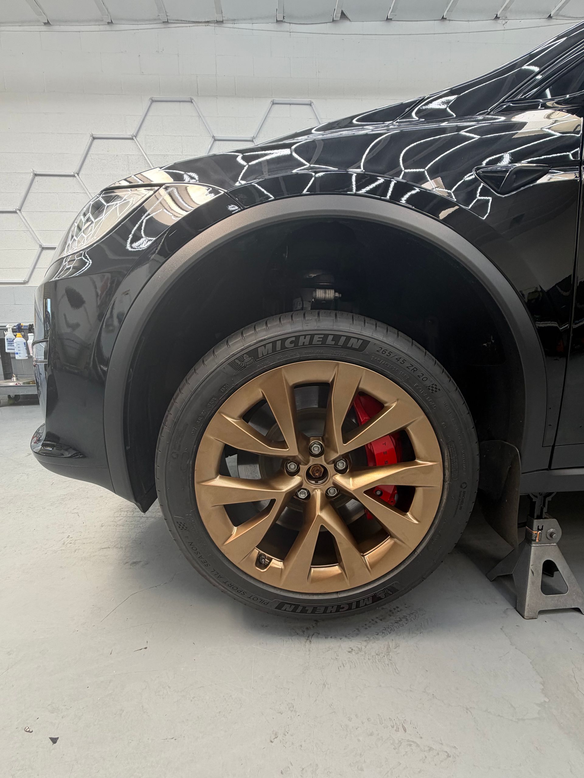 Black SUV front wheel with bronze rim and red brake caliper in a garage