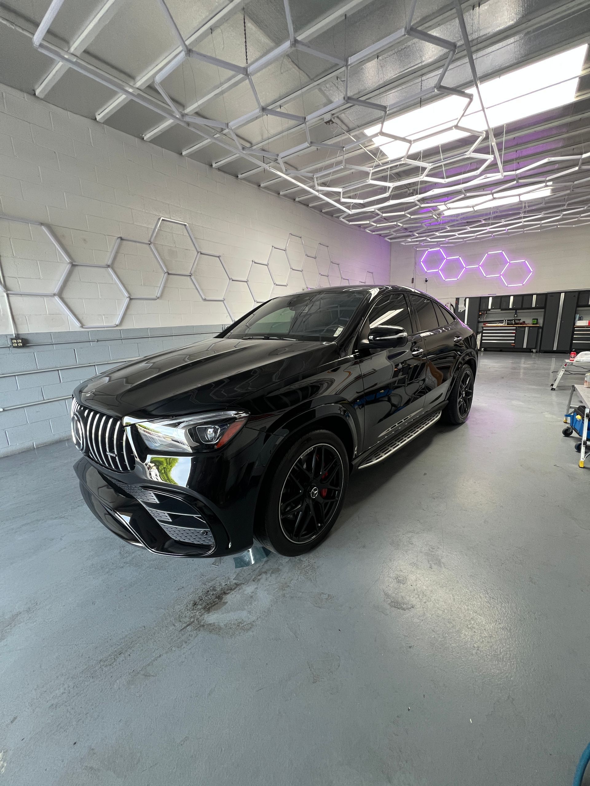 Black Mercedes SUV in a modern garage with hexagonal wall panels and neon lights