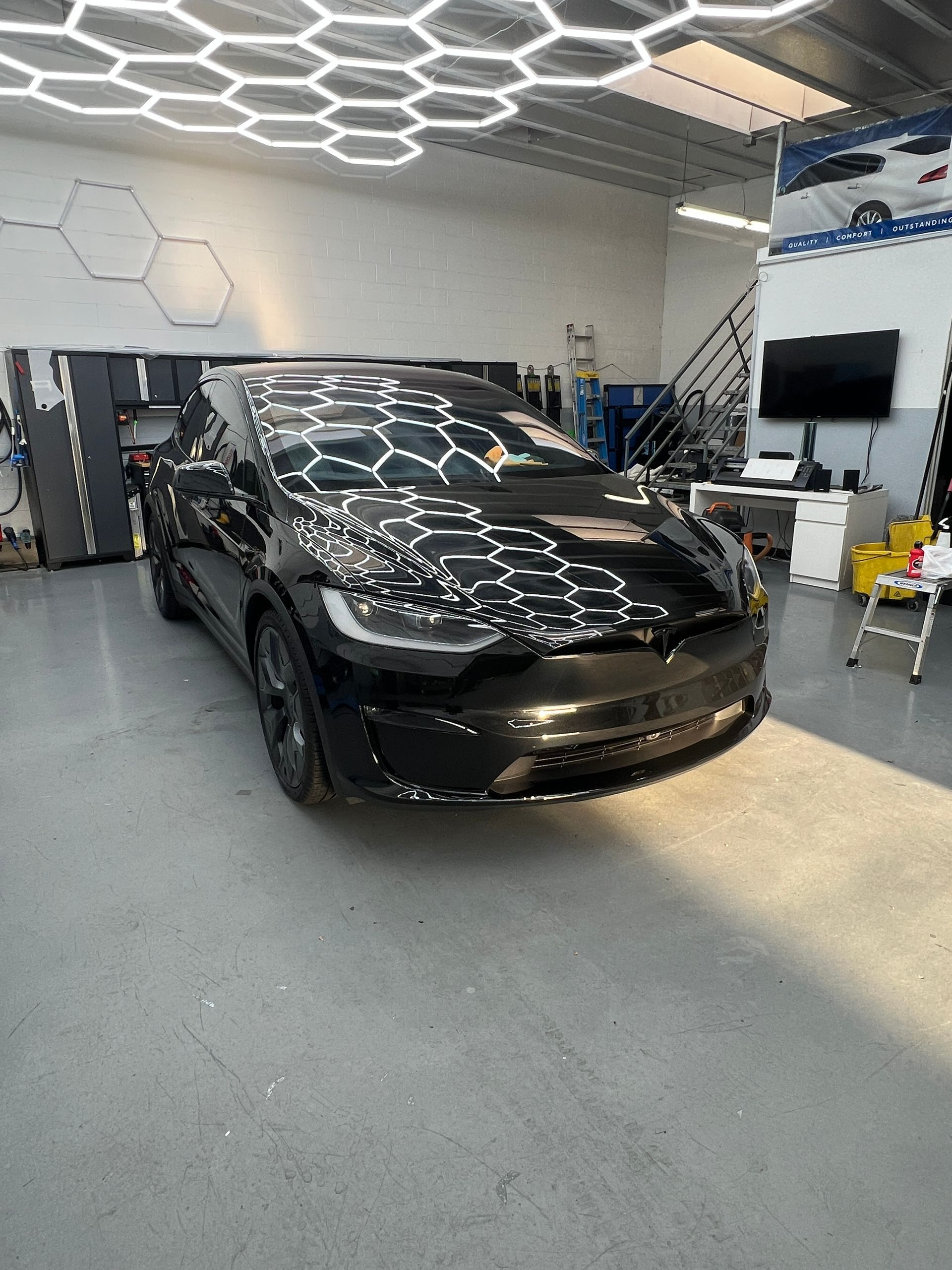 Black sports sedan in a bright auto shop with hexagonal ceiling lights reflected on the hood