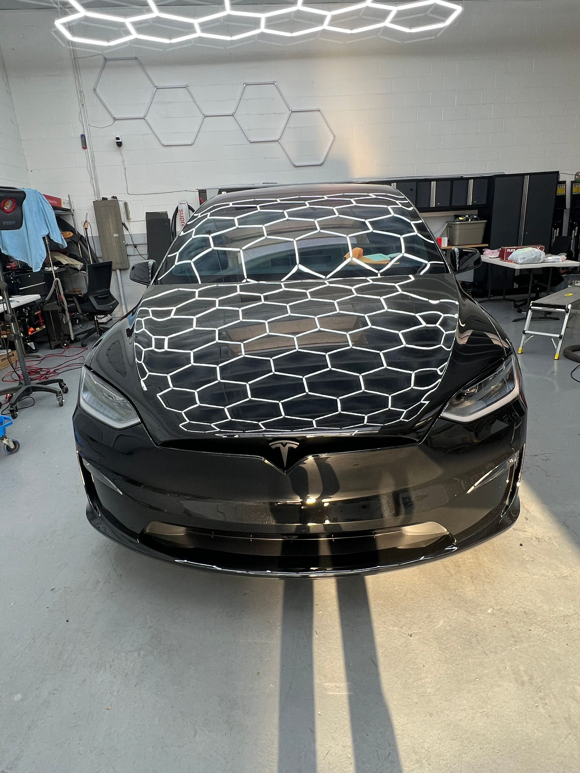 Black sports car in a garage, covered with a honeycomb-patterned wrap on the windshield and hood.