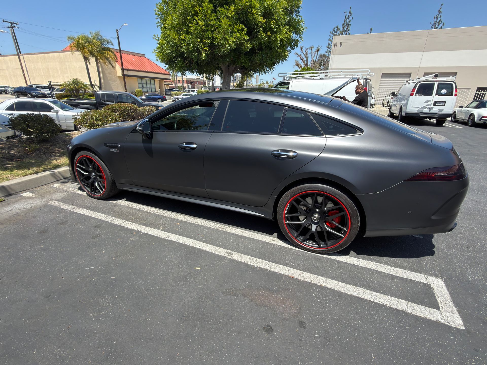 Dark gray sports sedan with red-rimmed wheels parked in a lot under bright sun.