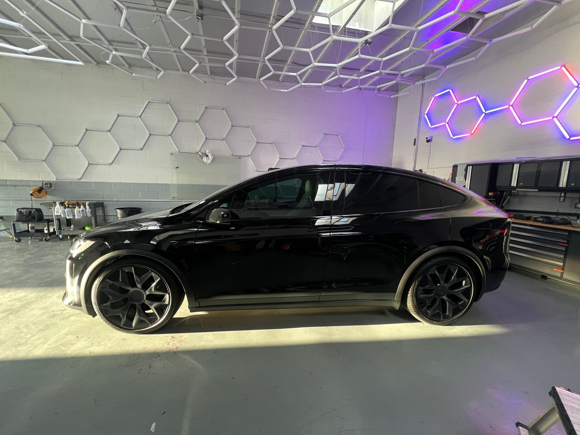 Black sports car in a modern showroom with geometric ceiling lights and neon wall accents