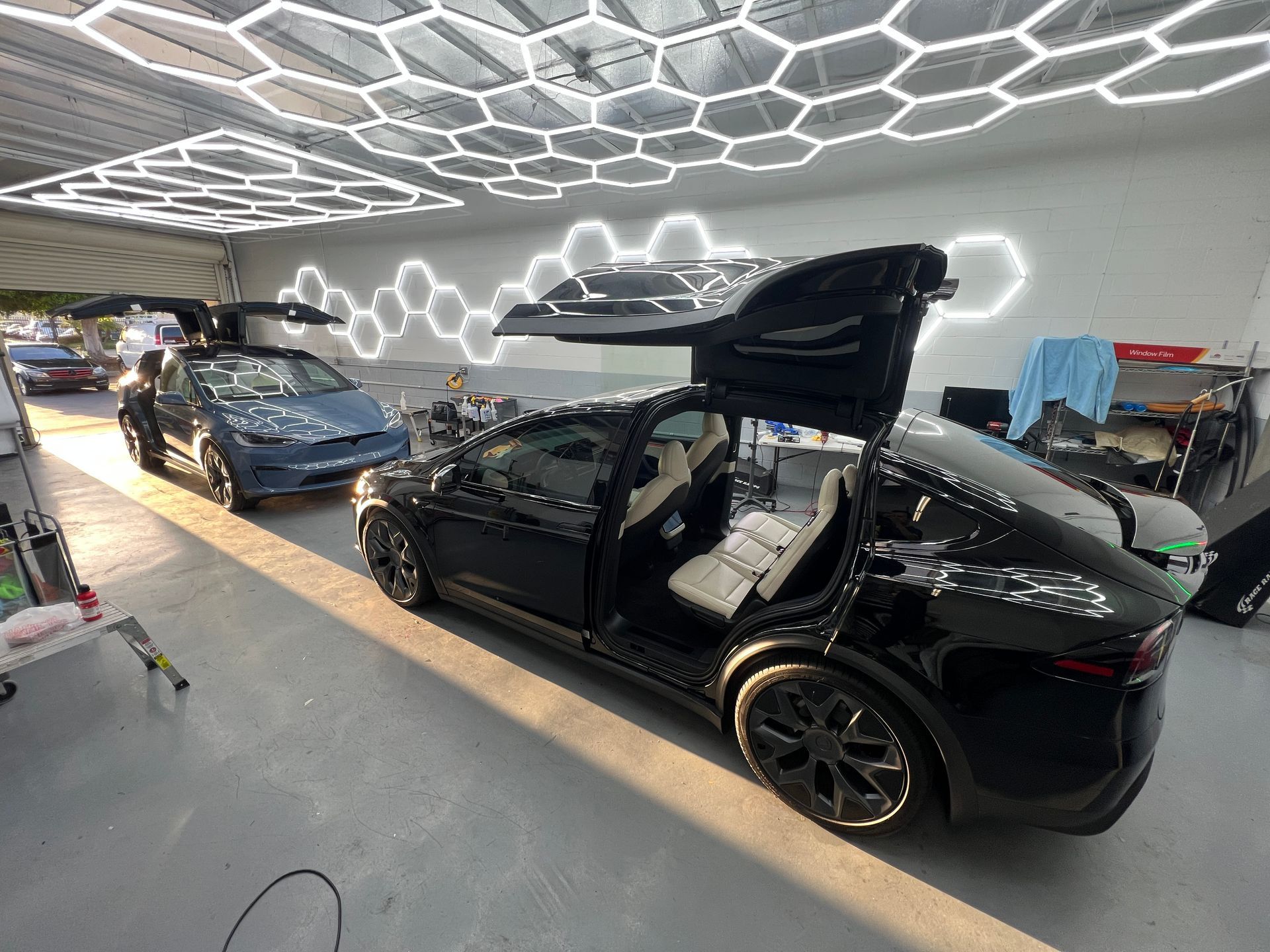 Two modified electric cars in a garage, one black with gullwing door and one blue near LED ceiling lights