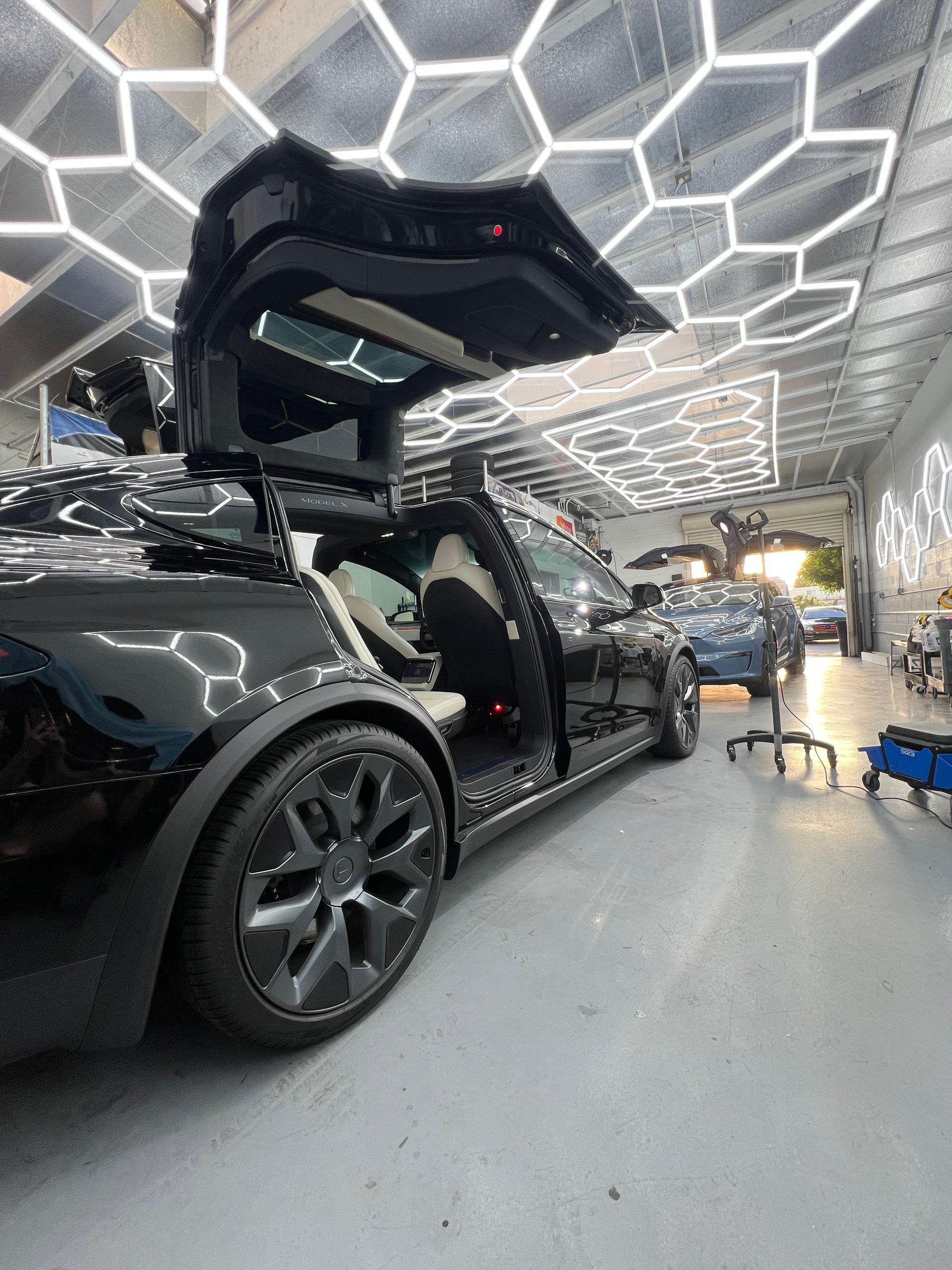 Black sports car with scissor door open in a futuristic showroom with hexagonal ceiling lights