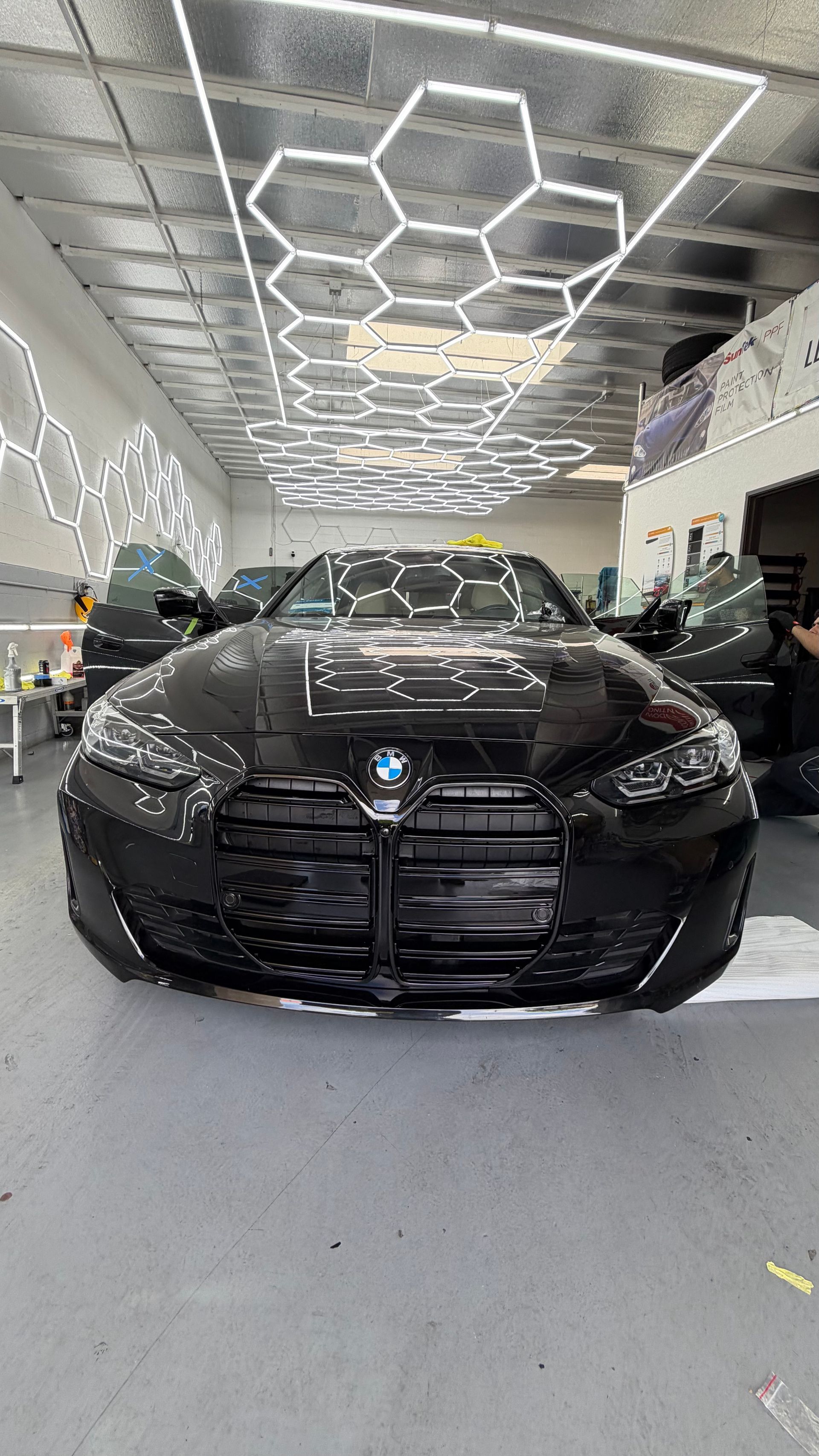 Black BMW sedan in a bright showroom with hexagonal ceiling lights reflected above.