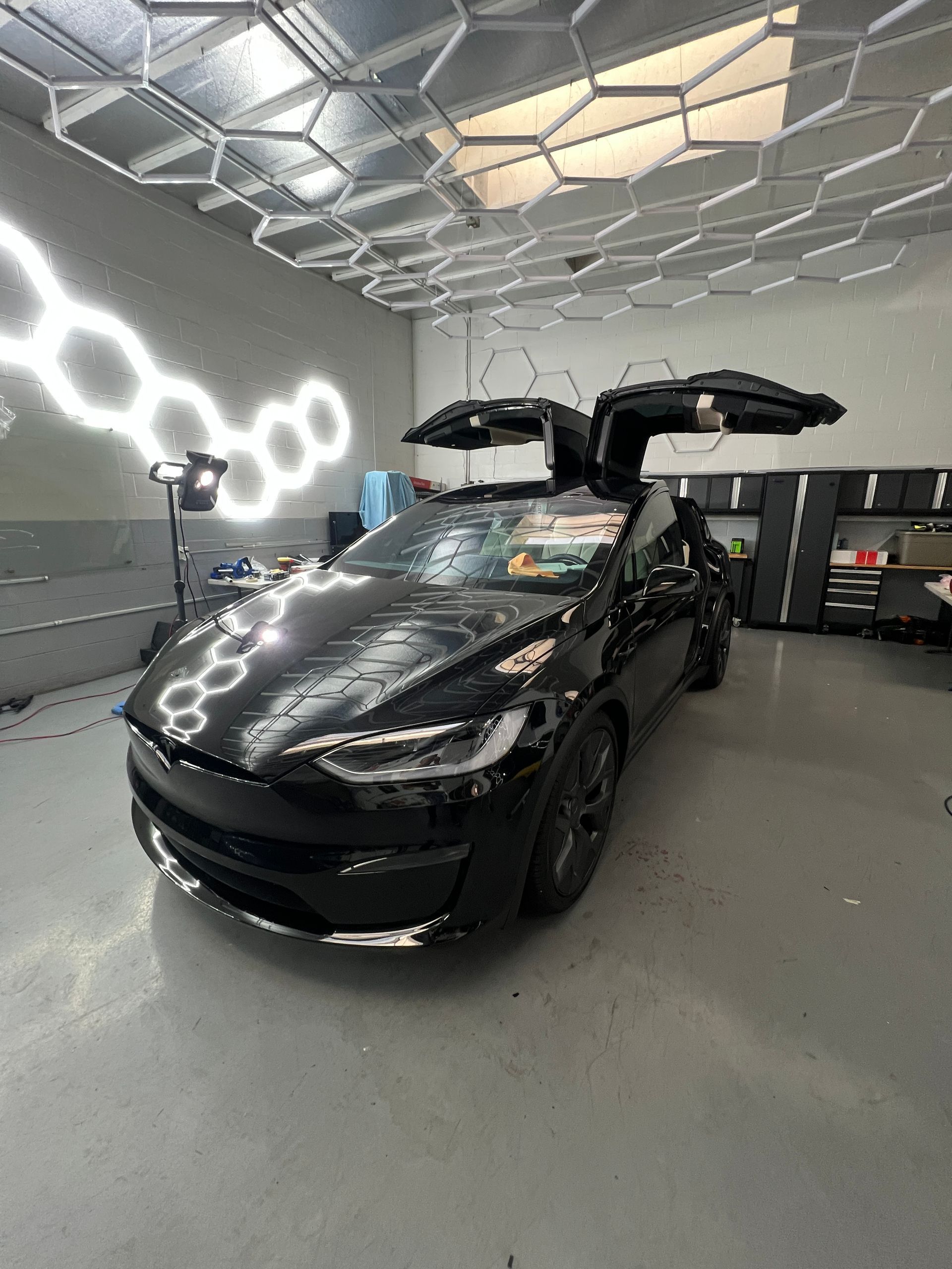 Black sports sedan with open doors in a modern garage with hexagonal ceiling lights and wall reflections