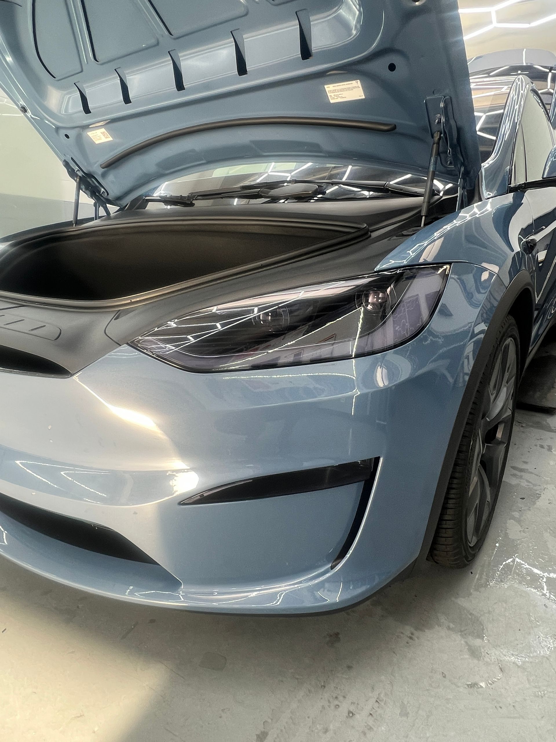Silver sedan with hood open in a garage, showing the front end and headlight
