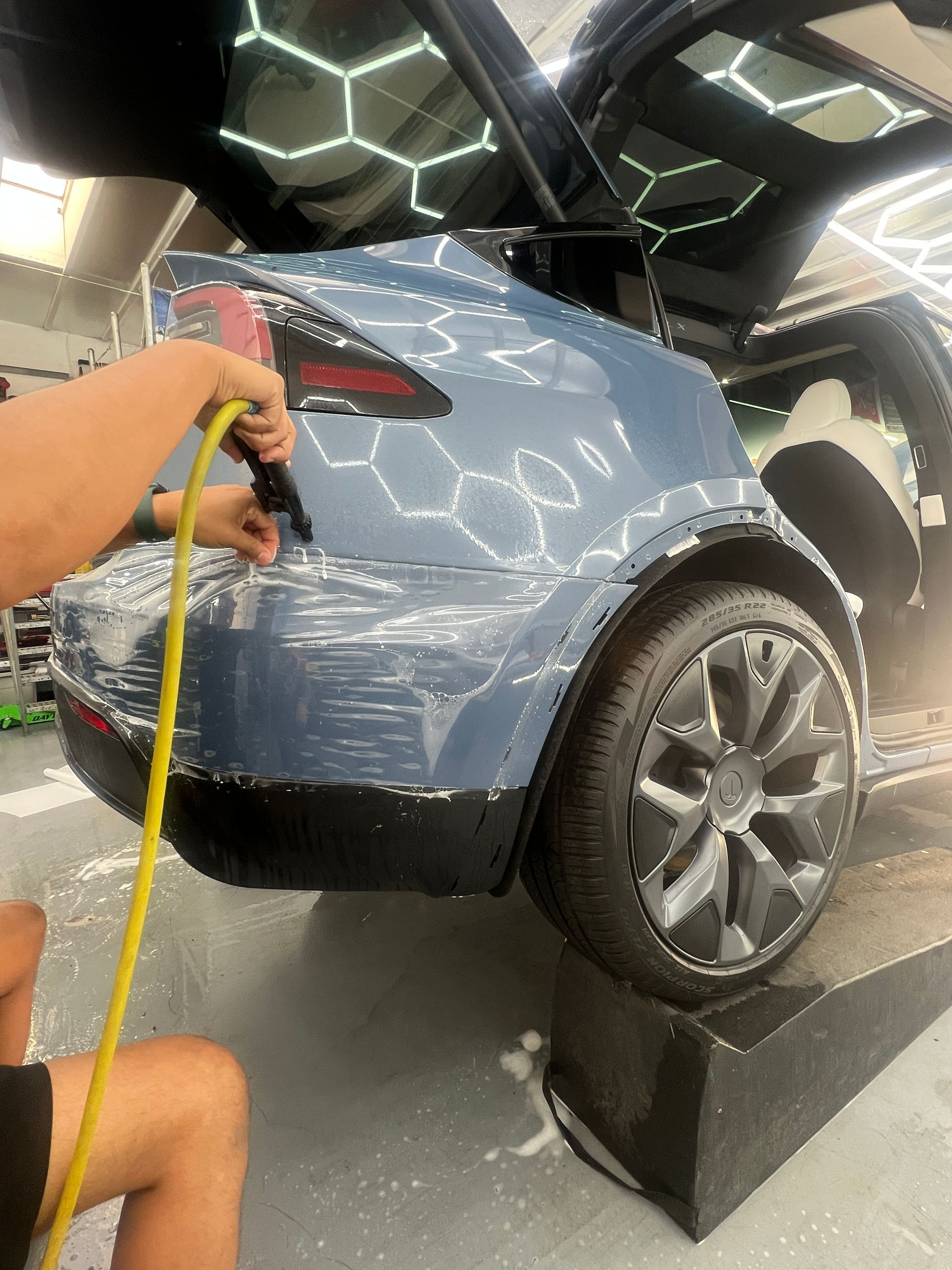 Blue car being washed with a yellow hose in a car detailing shop