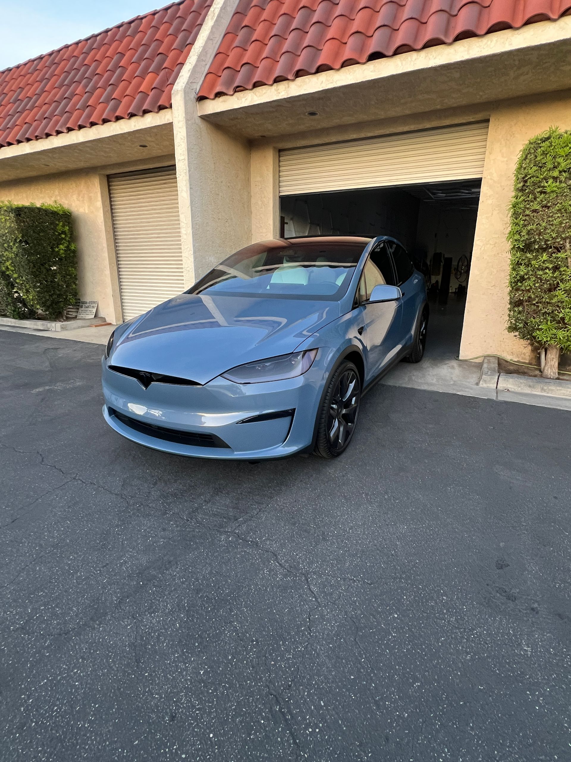 Blue Tesla parked in front of a tan garage with a red-tile roof