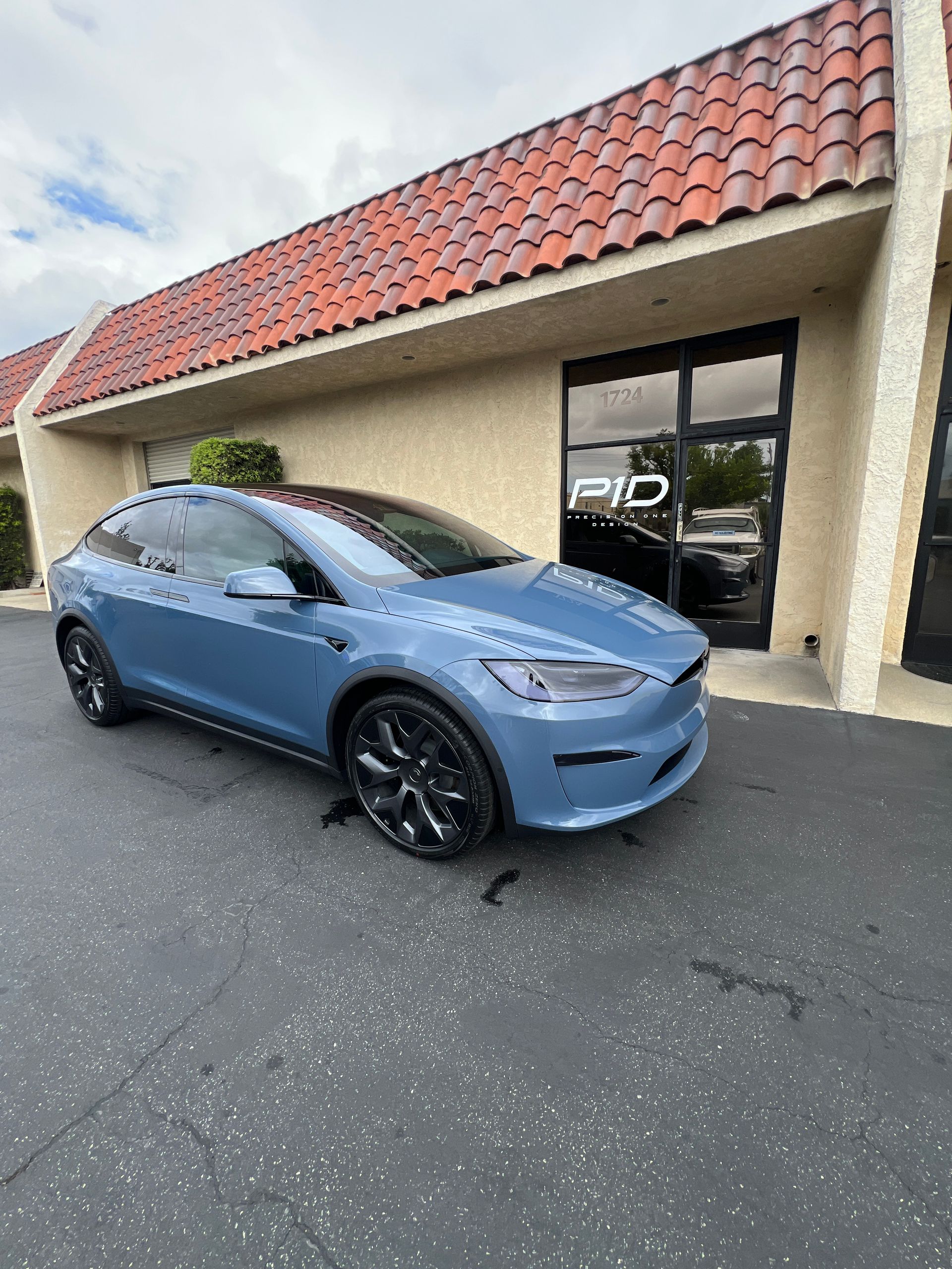 Blue Tesla parked outside a beige storefront with a red tile roof