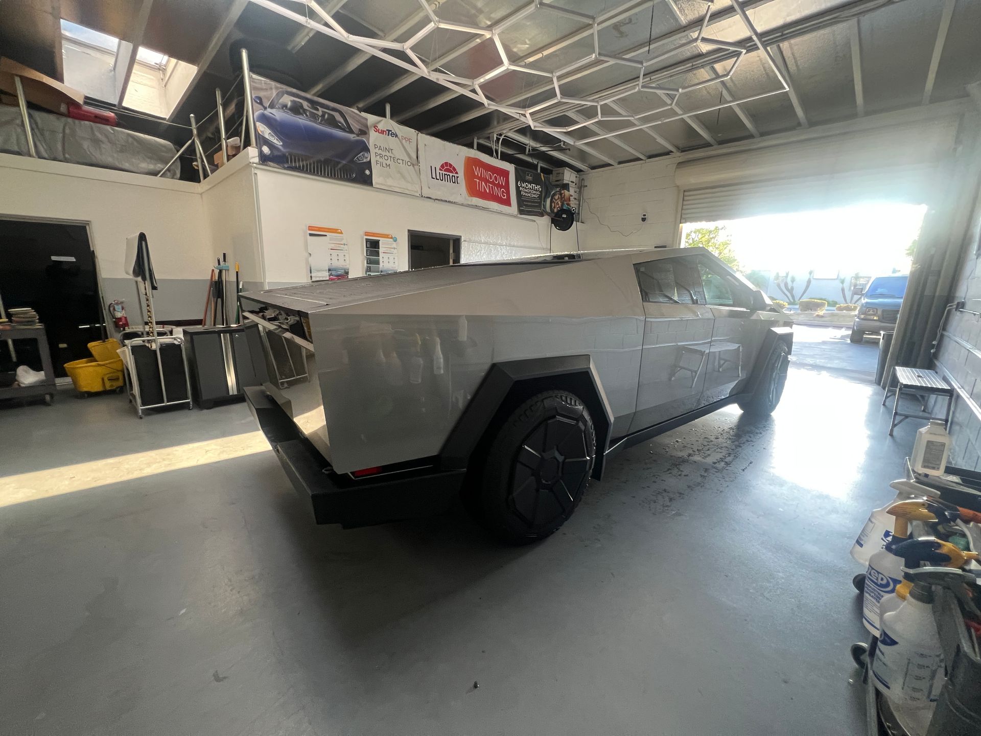 Gray futuristic pickup truck inside an auto shop garage with large open door and equipment around it
