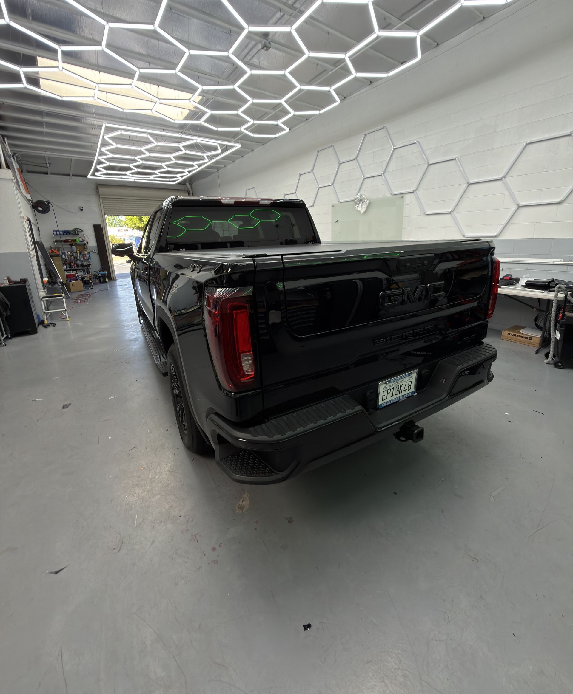 Black pickup truck parked inside a modern garage with hexagonal ceiling lights.