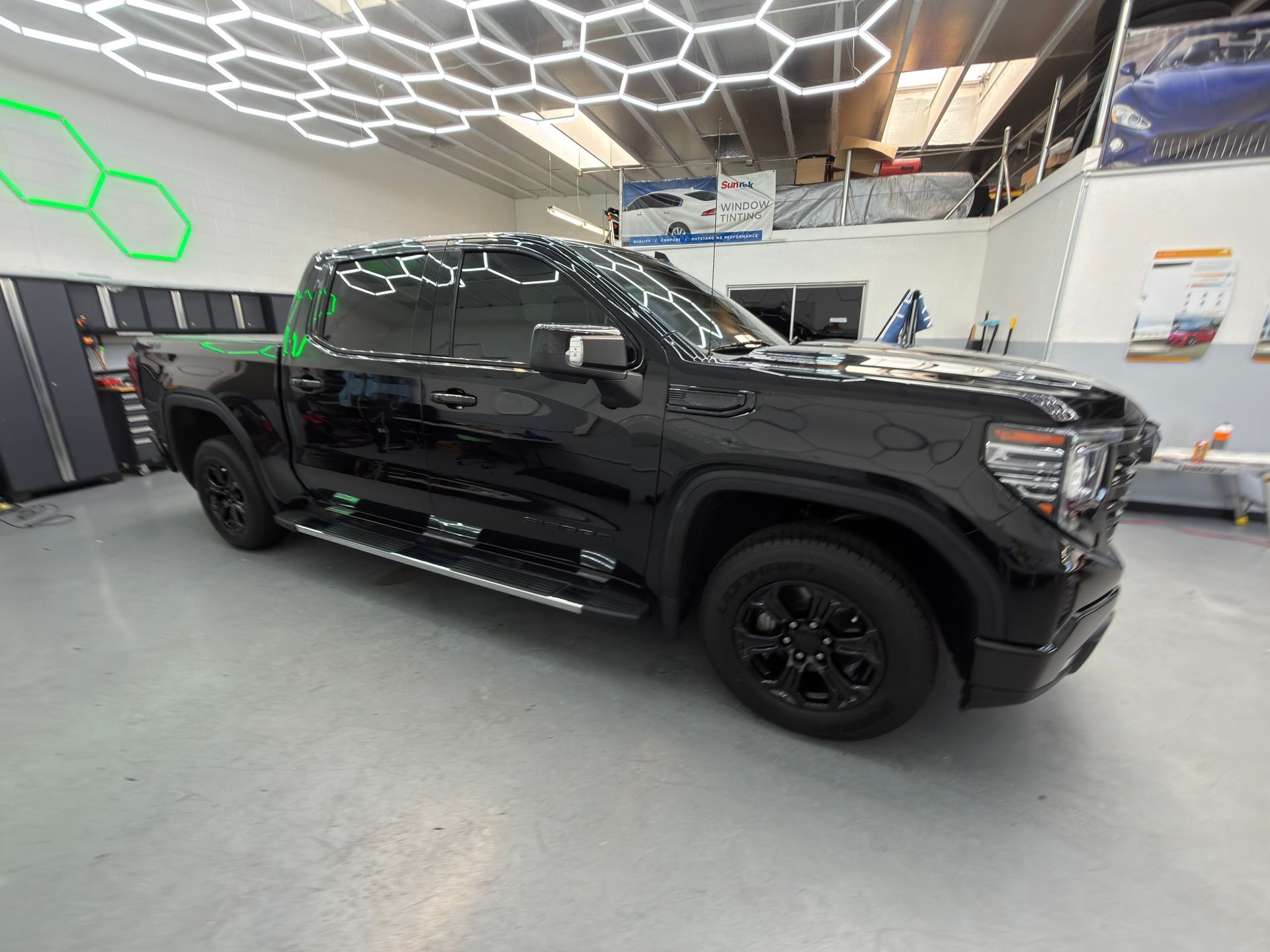 Black pickup truck in a showroom with hexagonal ceiling lights and a glossy floor