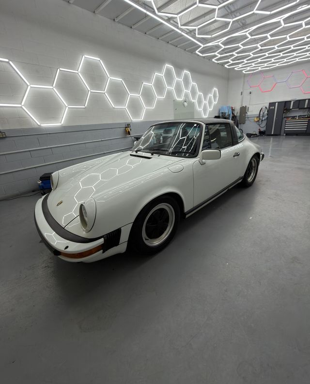 White classic Porsche 911 parked in a modern garage with glowing hexagonal wall lights