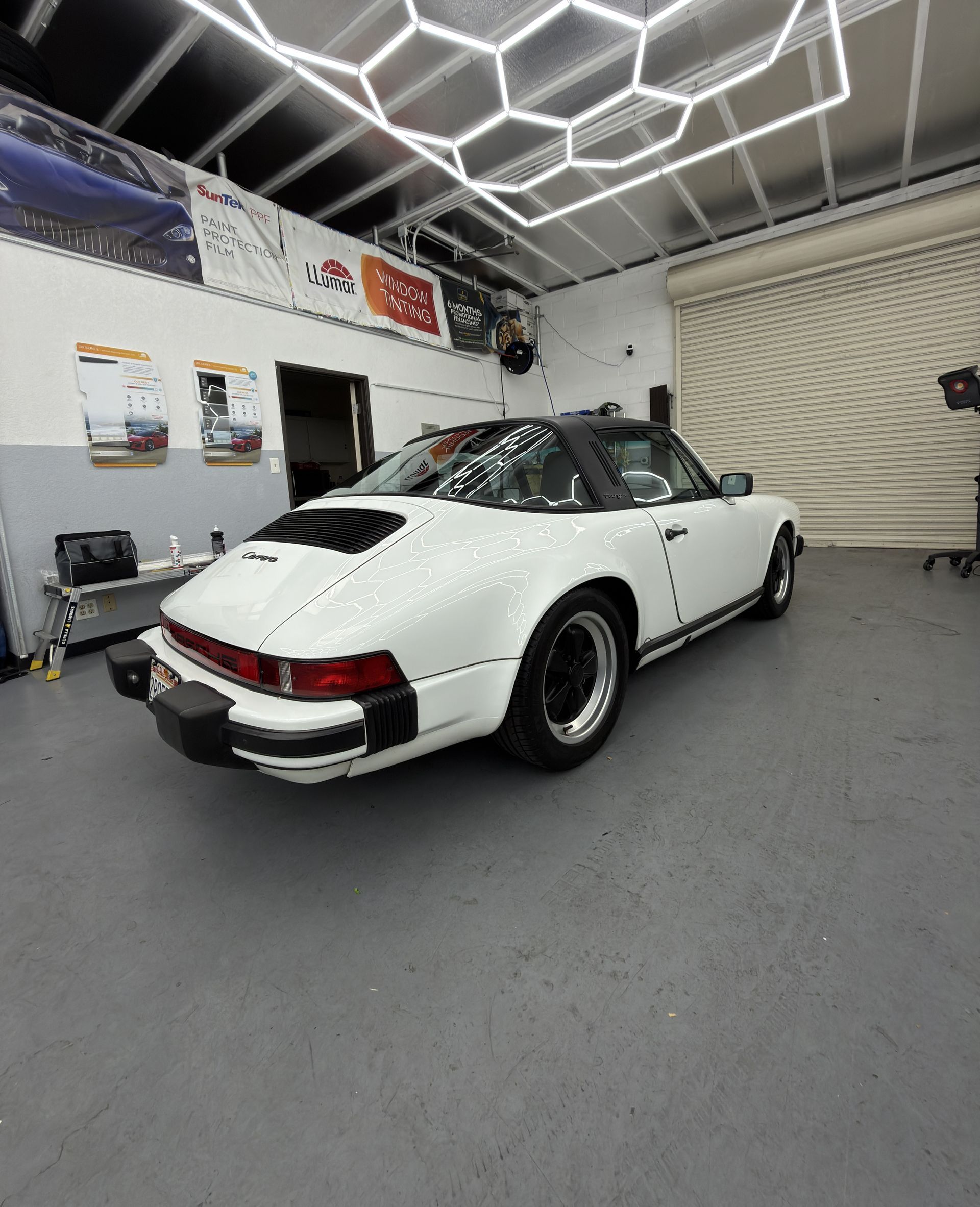 White classic Porsche 911 in a garage with hexagon ceiling lights and a rolled-up door