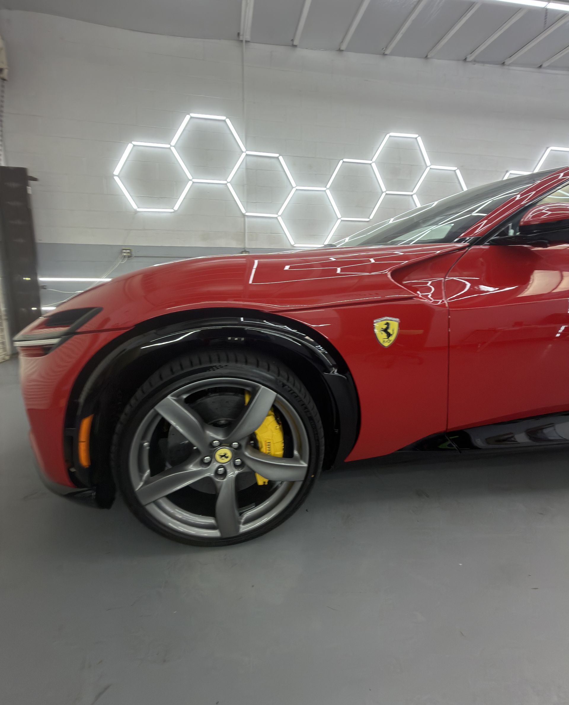 Red Ferrari sports car in a showroom, close-up of front wheel and fender under hexagonal wall lights