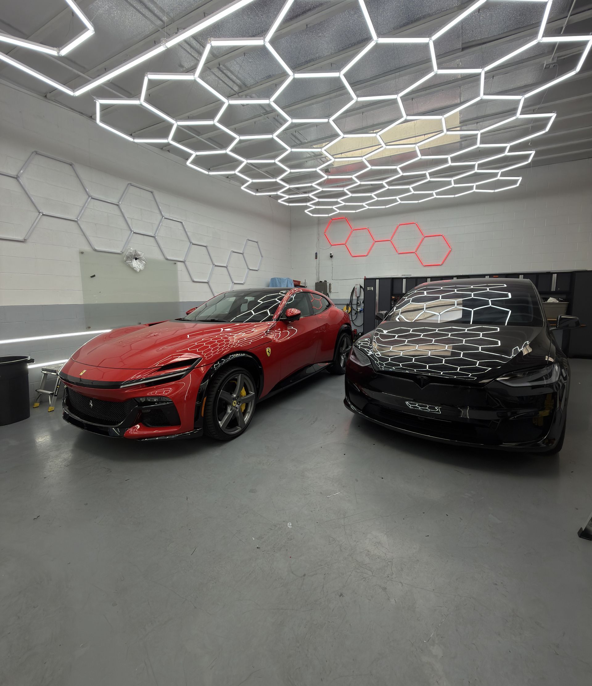 Red and black sports cars parked in a modern showroom with hexagonal ceiling lights.