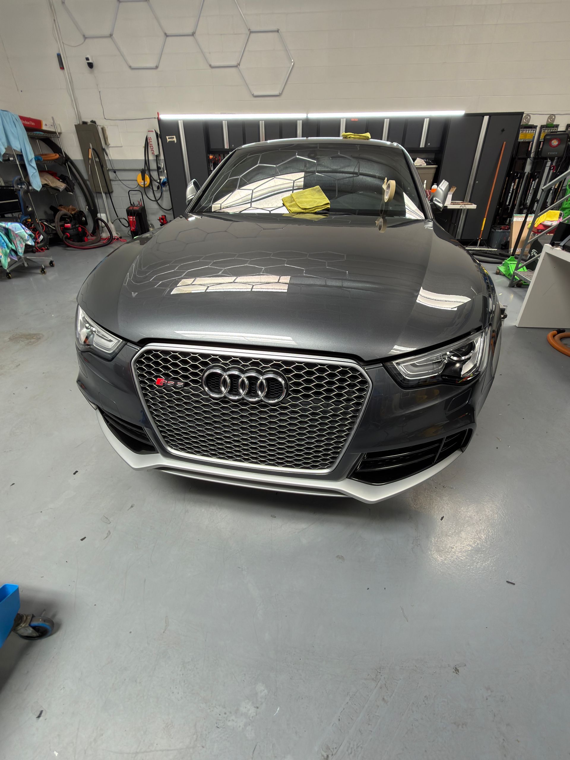 Gray Audi sedan in a garage, front view with hood open and a yellow cloth on the windshield.