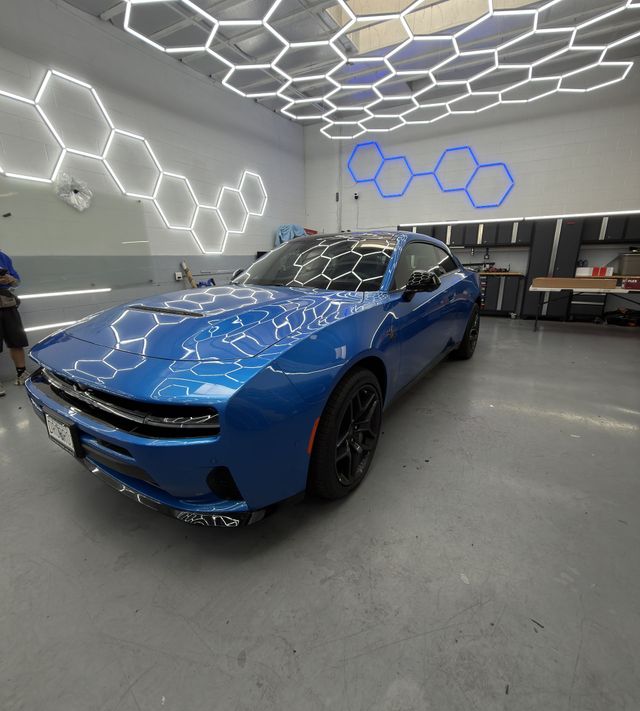 Blue sports sedan in a garage showroom with illuminated hexagon wall lights and ceiling panels