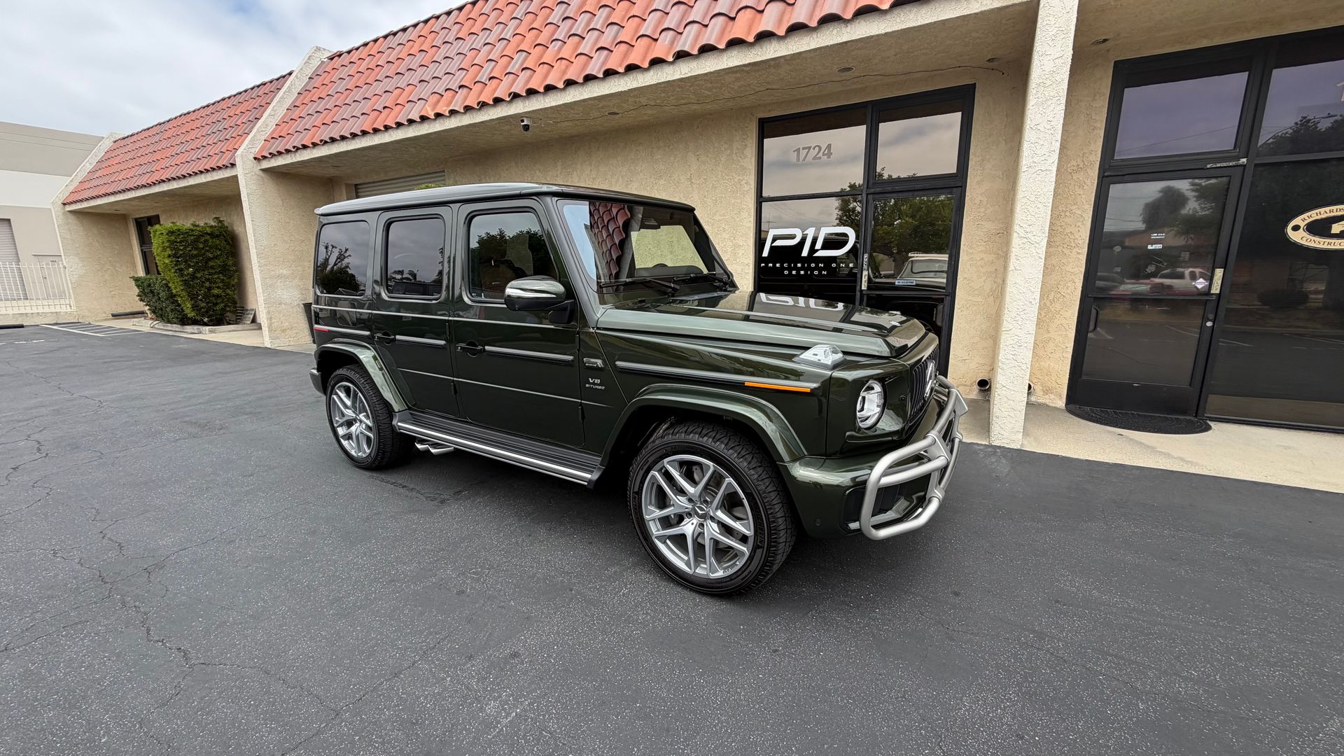 Dark green SUV parked outside a beige storefront with red roof tiles.