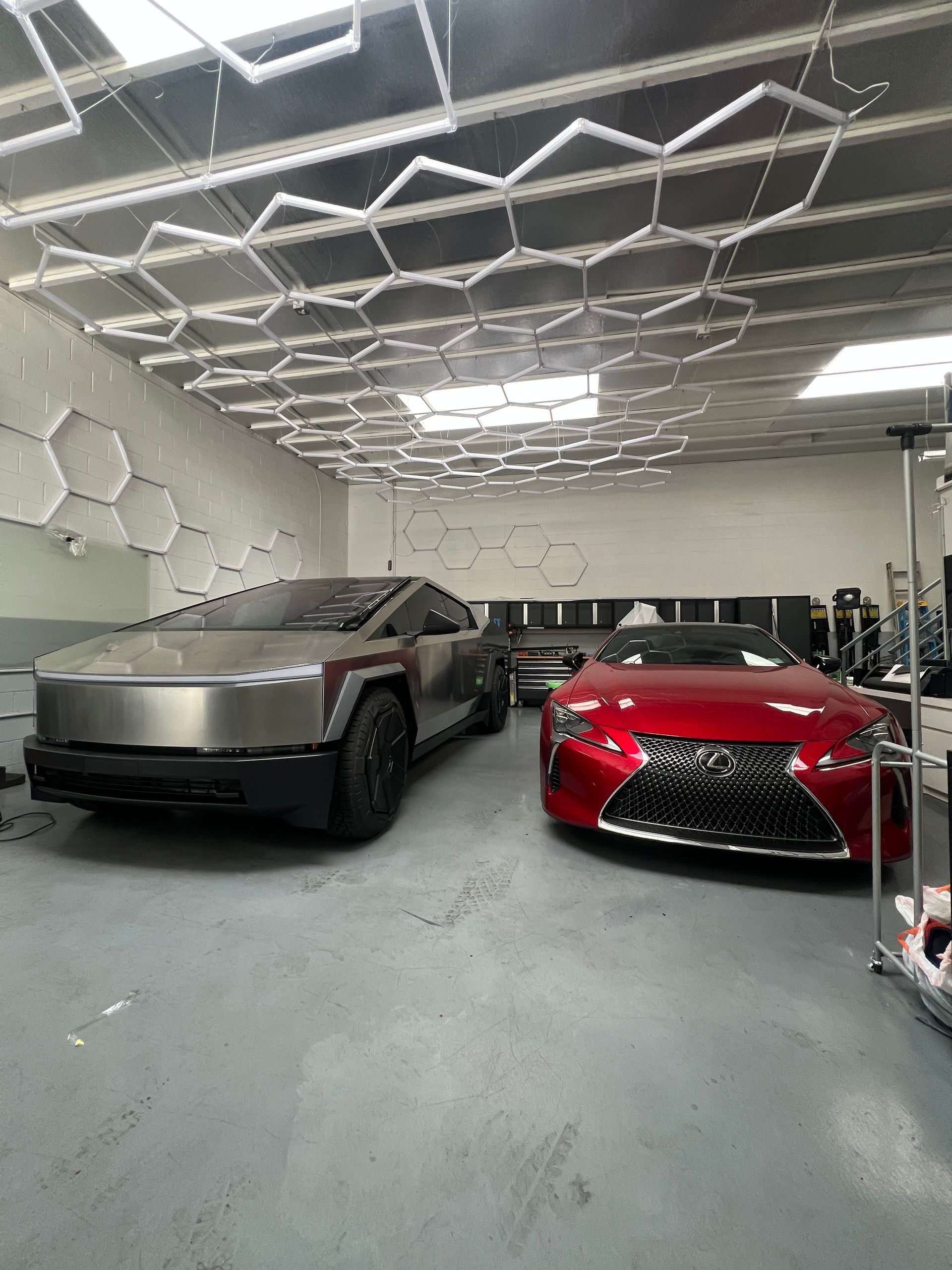 Two sports cars parked in a modern garage, one matte gray and one red, under geometric ceiling lights