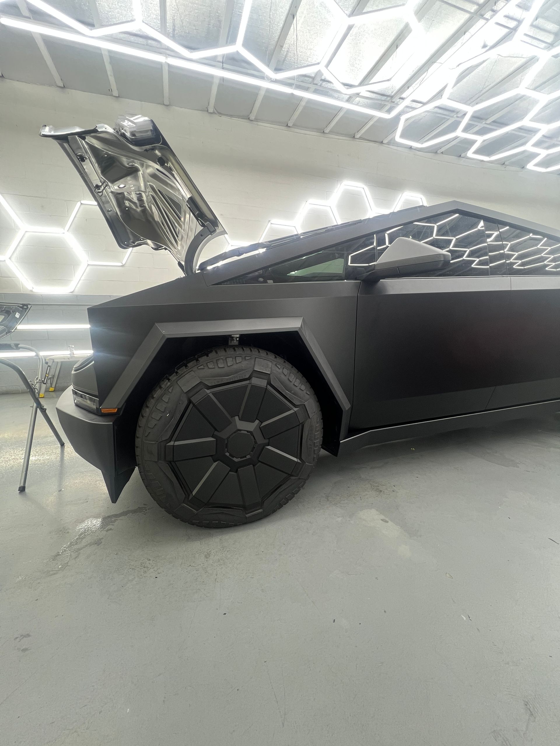 Black angular Cybertruck with open rear hatch in a bright showroom, side view.