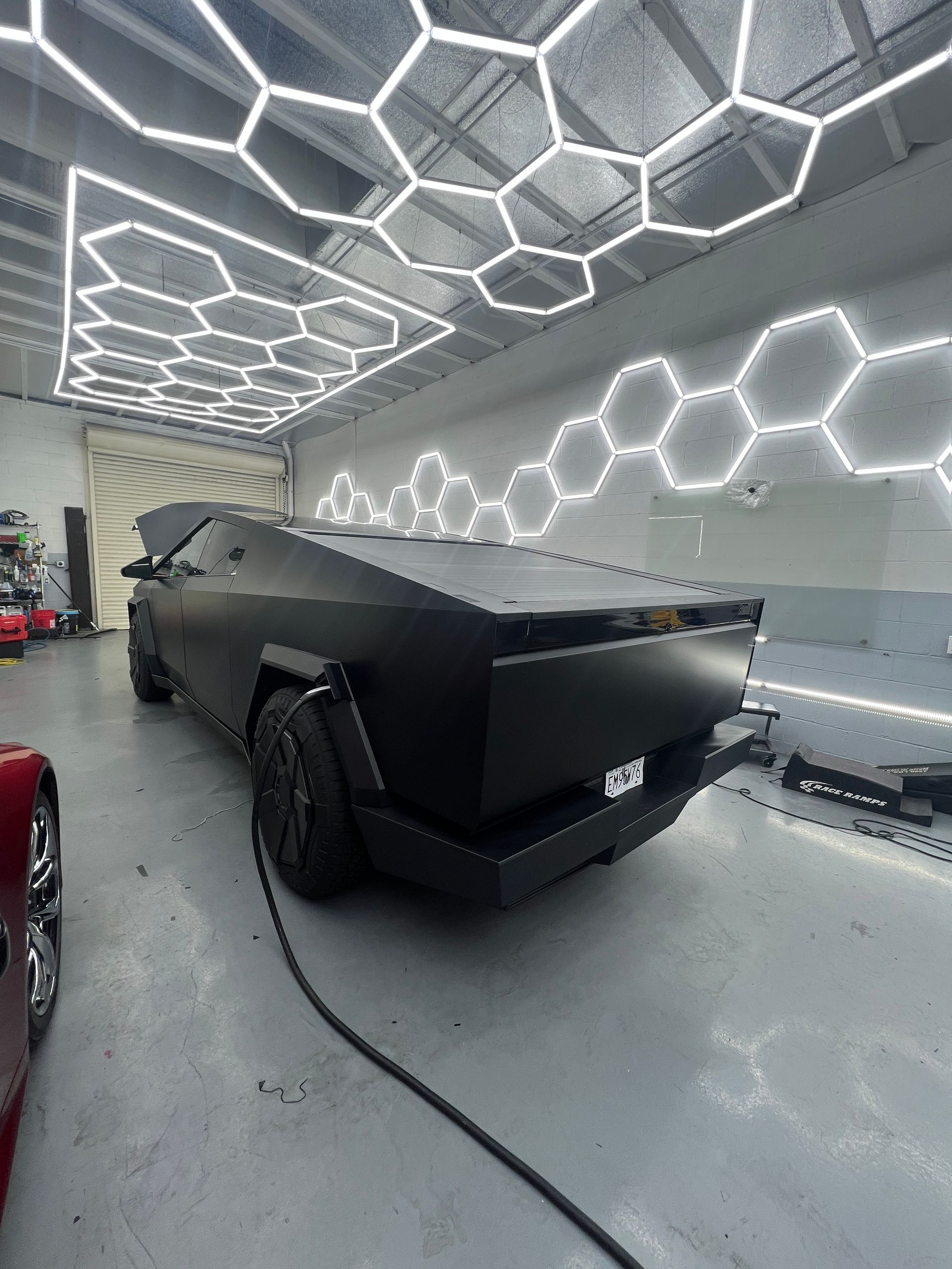 Matte black Cybertruck in a garage with bright hexagonal LED ceiling lights