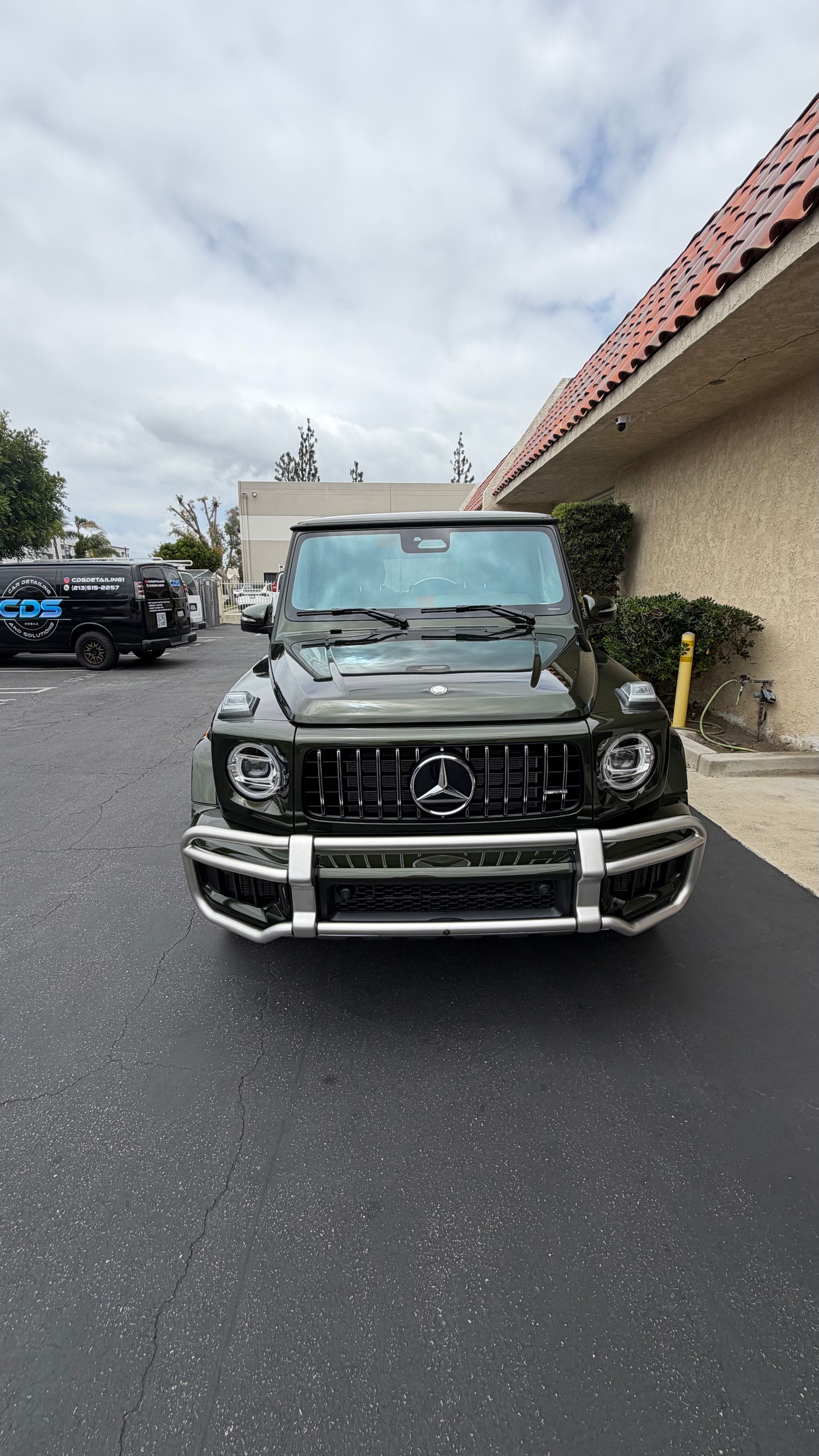 Front view of a black Jeep SUV parked on a street beside a beige building under cloudy skies