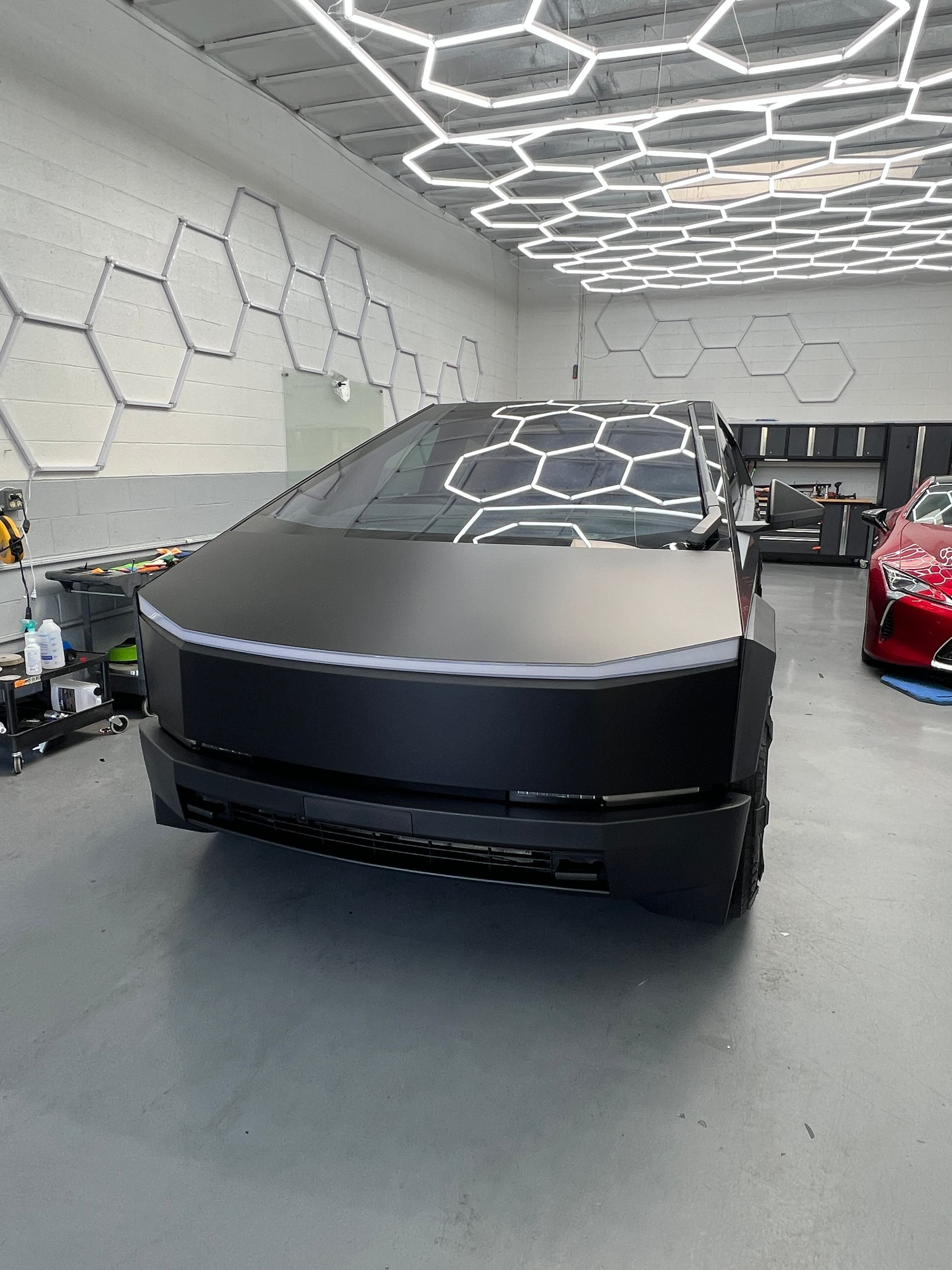 Matte black Tesla Cybertruck in a modern showroom with hexagonal wall lighting