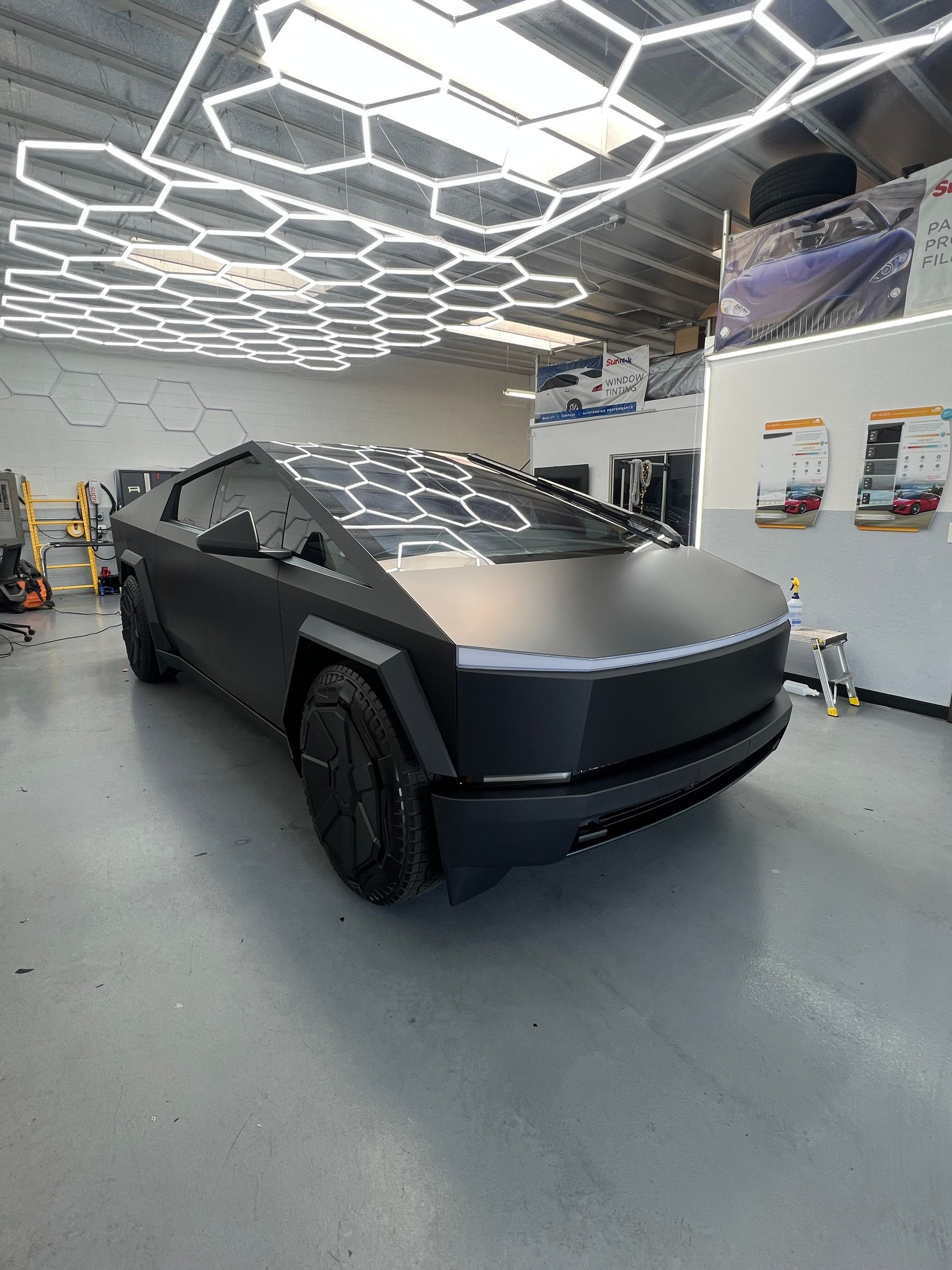 Futuristic matte black Tesla Cybertruck in a workshop with geometric ceiling lights