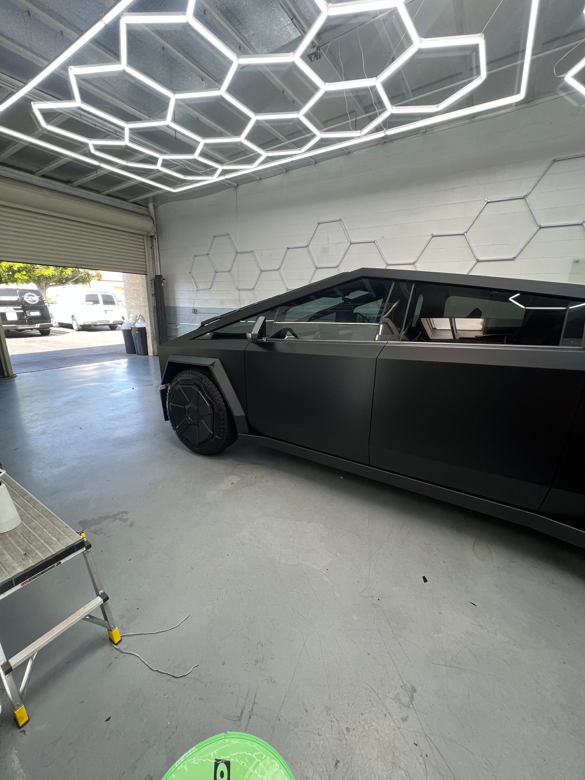 Black sports car parked inside a garage with hexagonal LED ceiling lights.