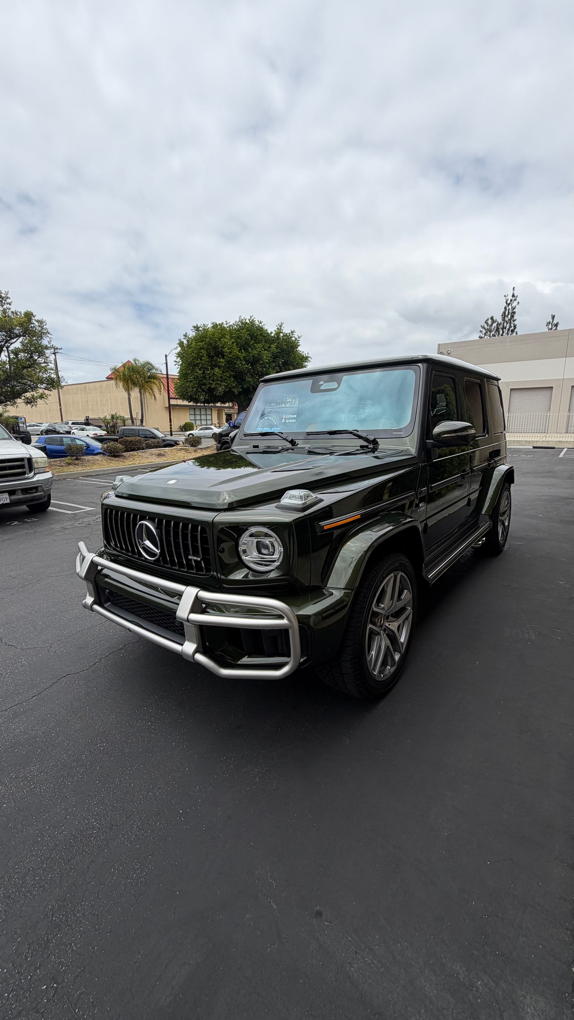 Black Mercedes G-Class SUV parked on a wet street under cloudy skies