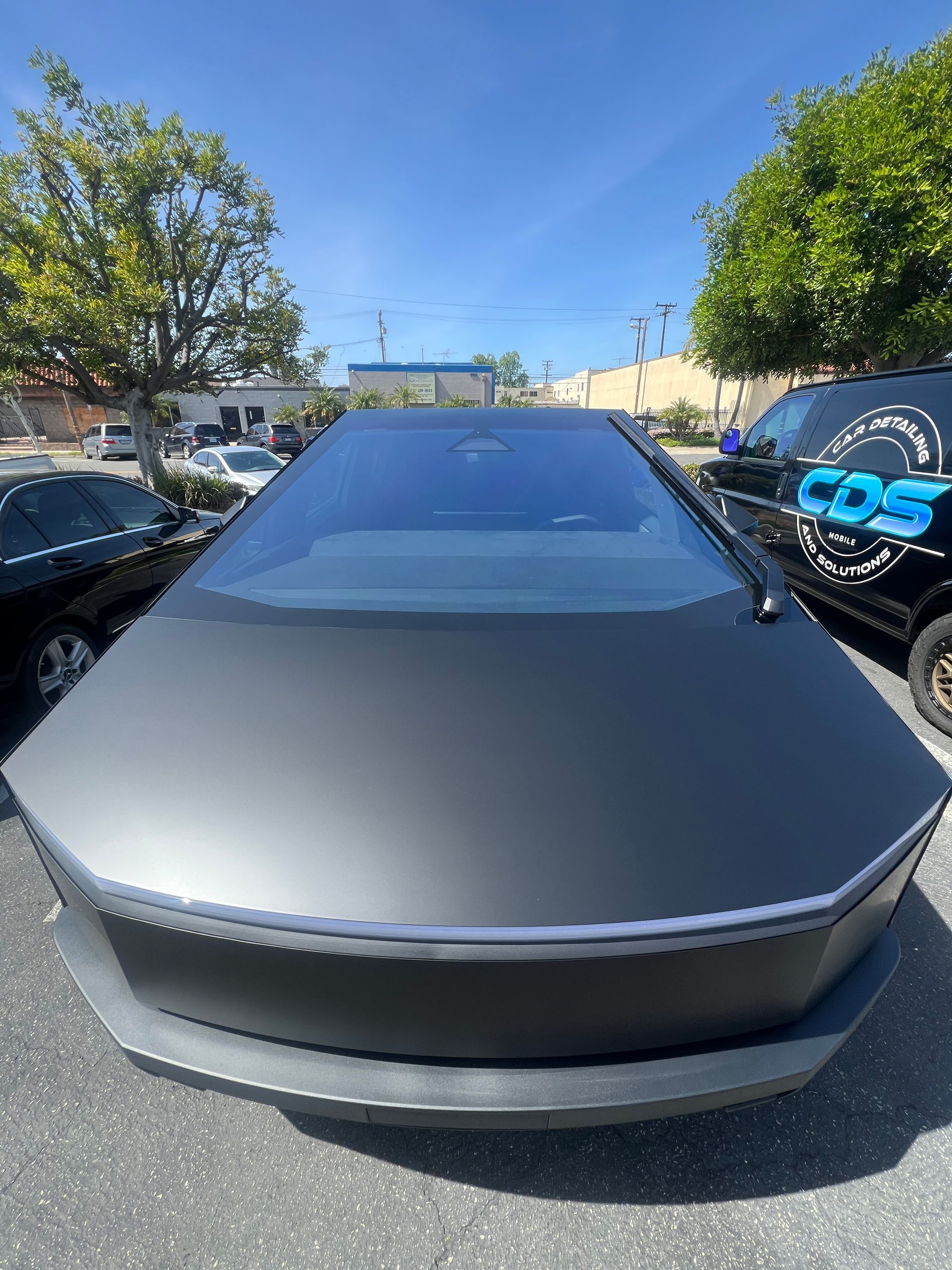 Front view of a gray Tesla parked outdoors between cars on a sunny day