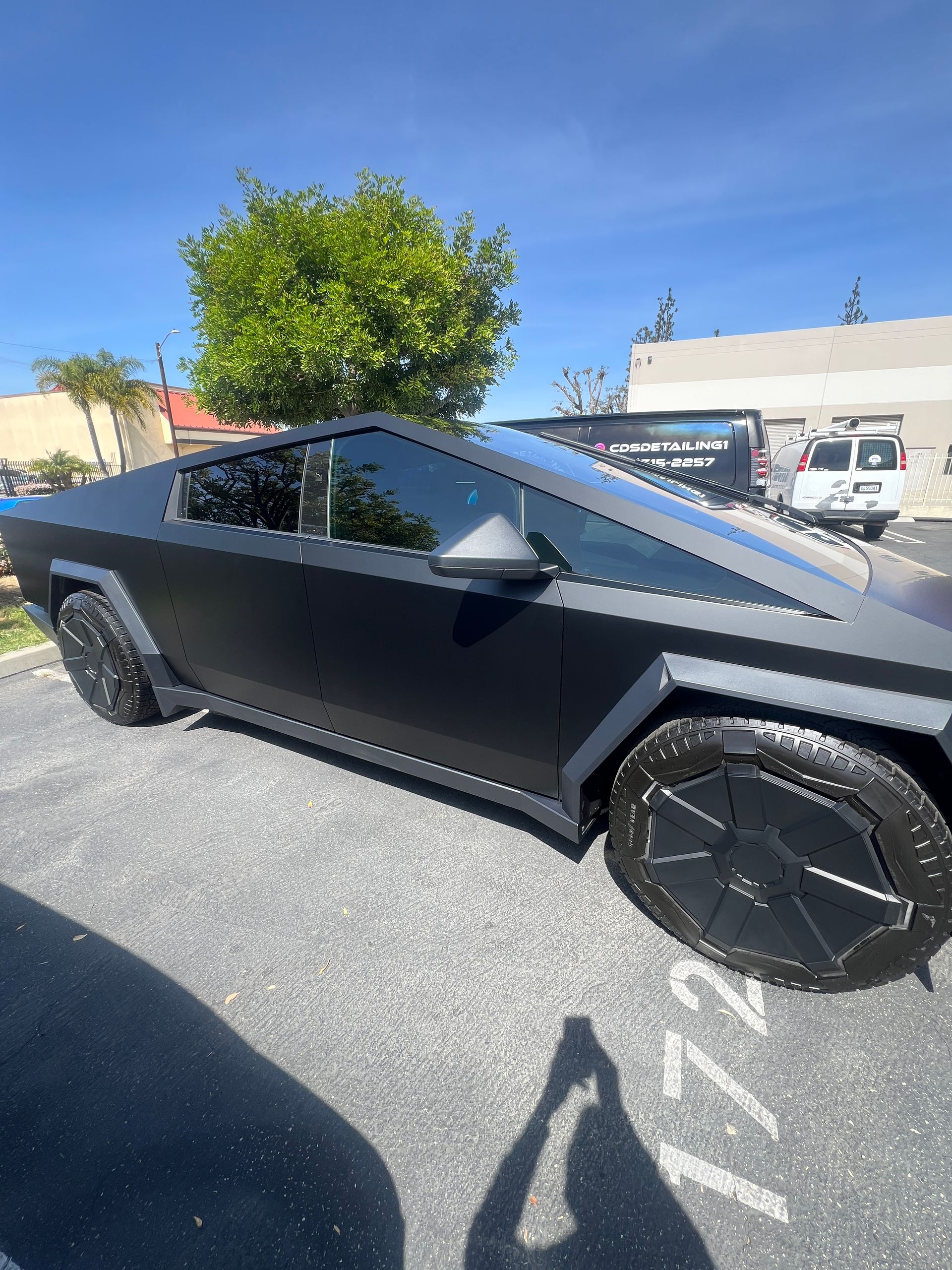 Matte black futuristic pickup truck parked in a lot under a blue sky