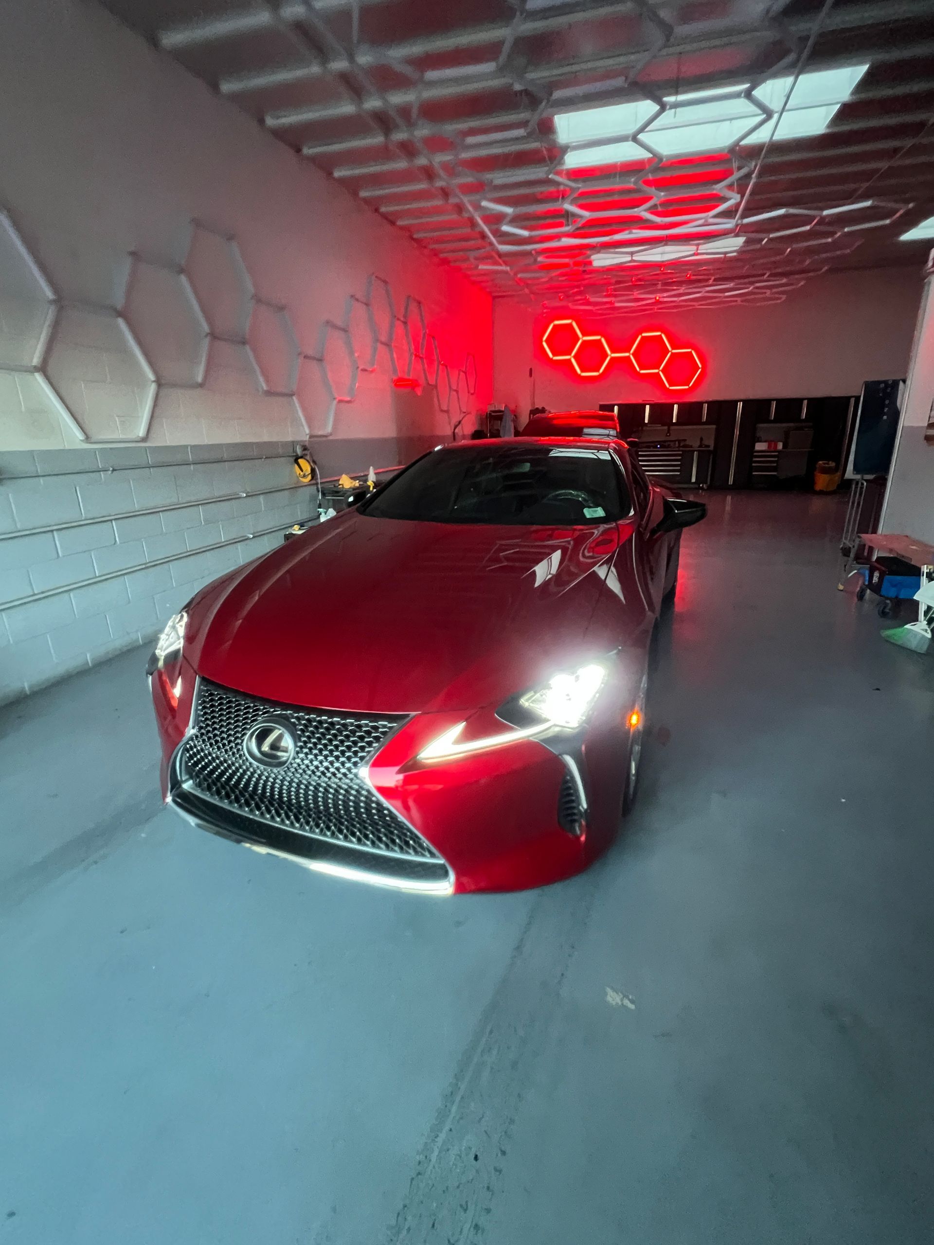 Red Lexus sedan in a garage with red neon lights and hexagonal wall decor.
