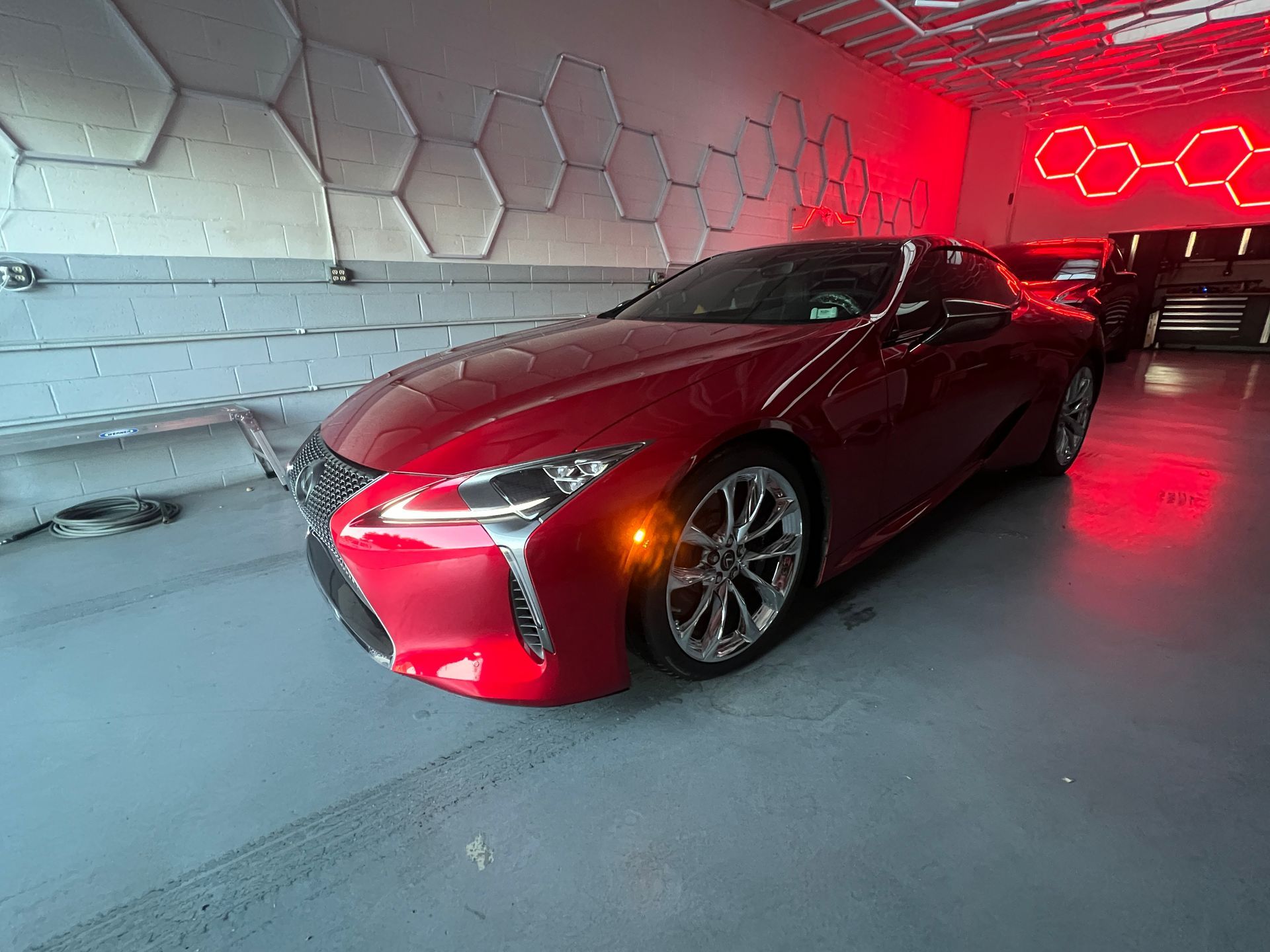 Red sports car in a modern garage with hexagonal wall lights and red neon glow
